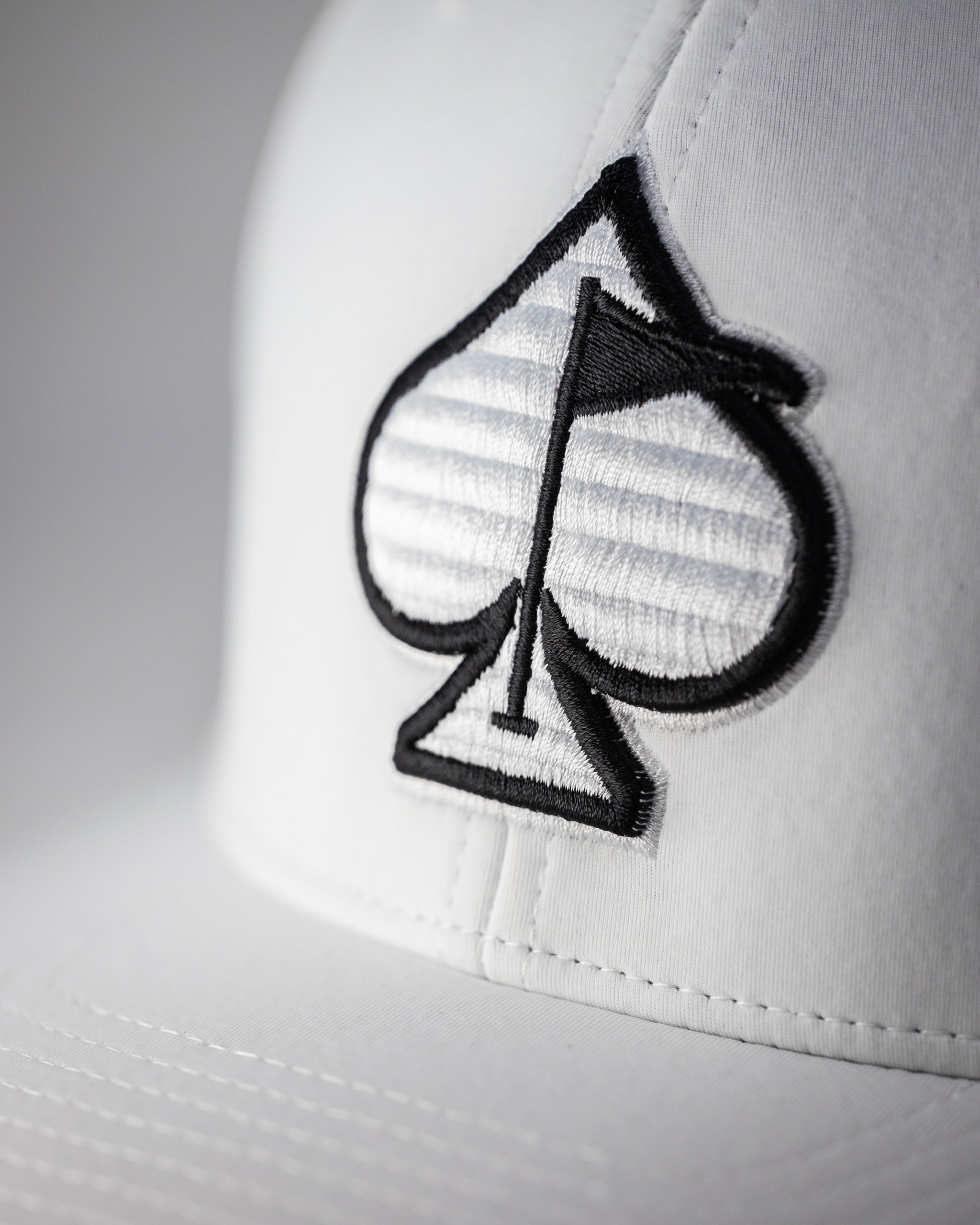 White Performance Spade Hat featuring a bold black spade logo, designed for stylish golfers seeking standout accessories.