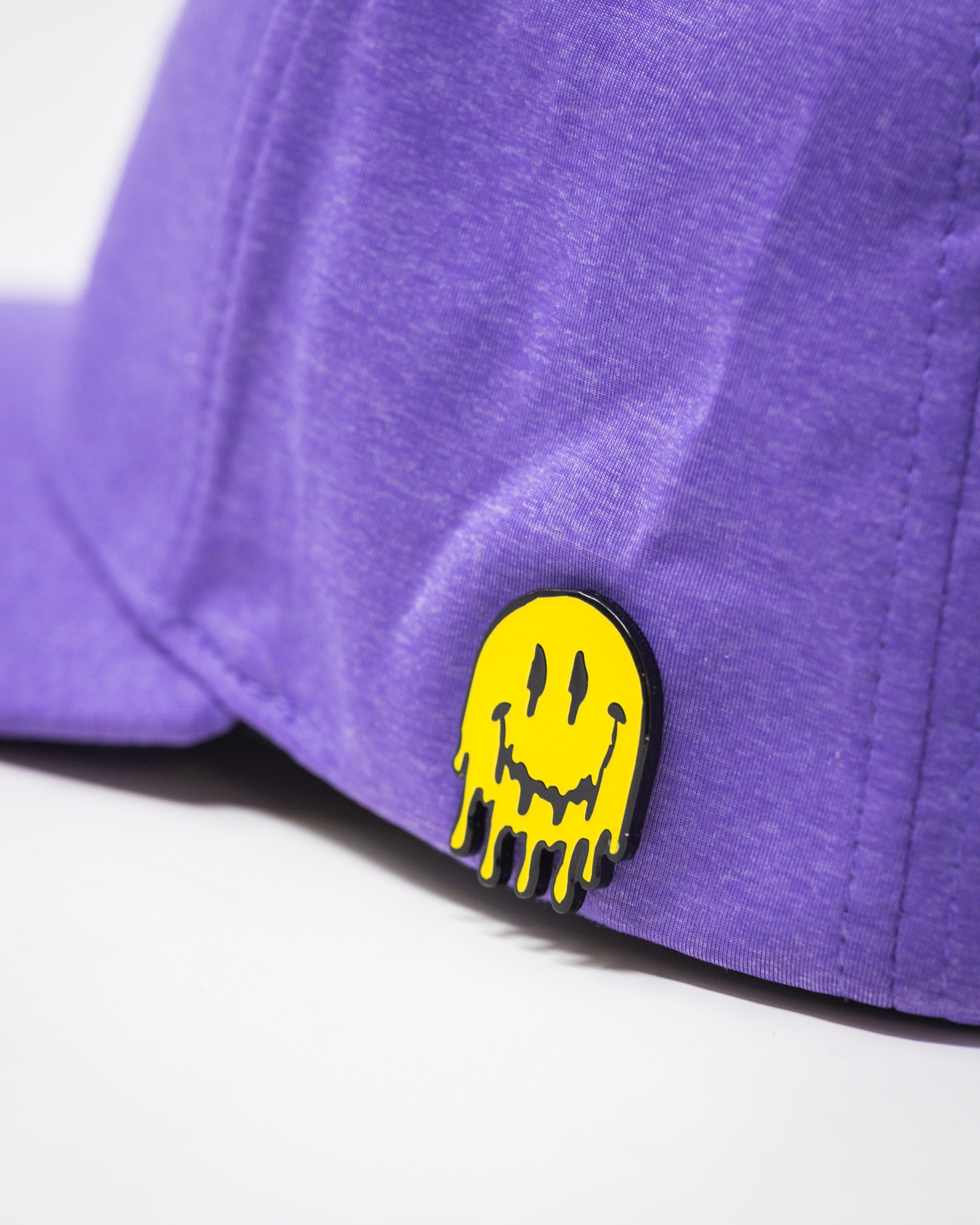 Lavender performance hat featuring a playful yellow dripping smiley face pin on the front. Ideal for stylish golfers.