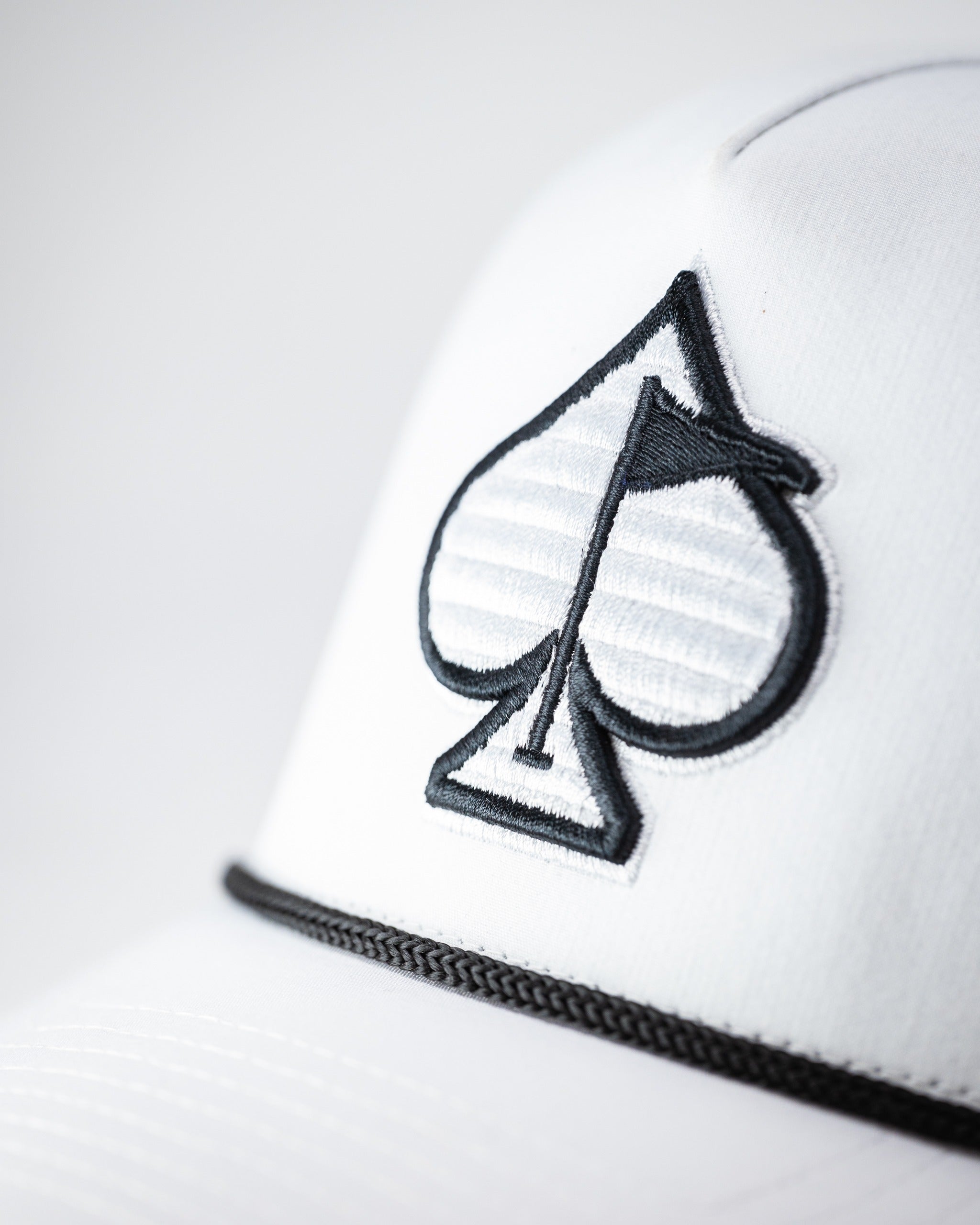 White perforated rope hat featuring a black spade logo and stylish trim, perfect for bold golfers on the course.