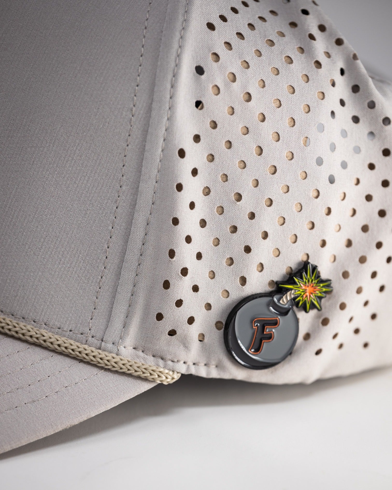 Perforated rope hat in bone color featuring a stylish design and a unique logo pin for a standout look on the golf course.