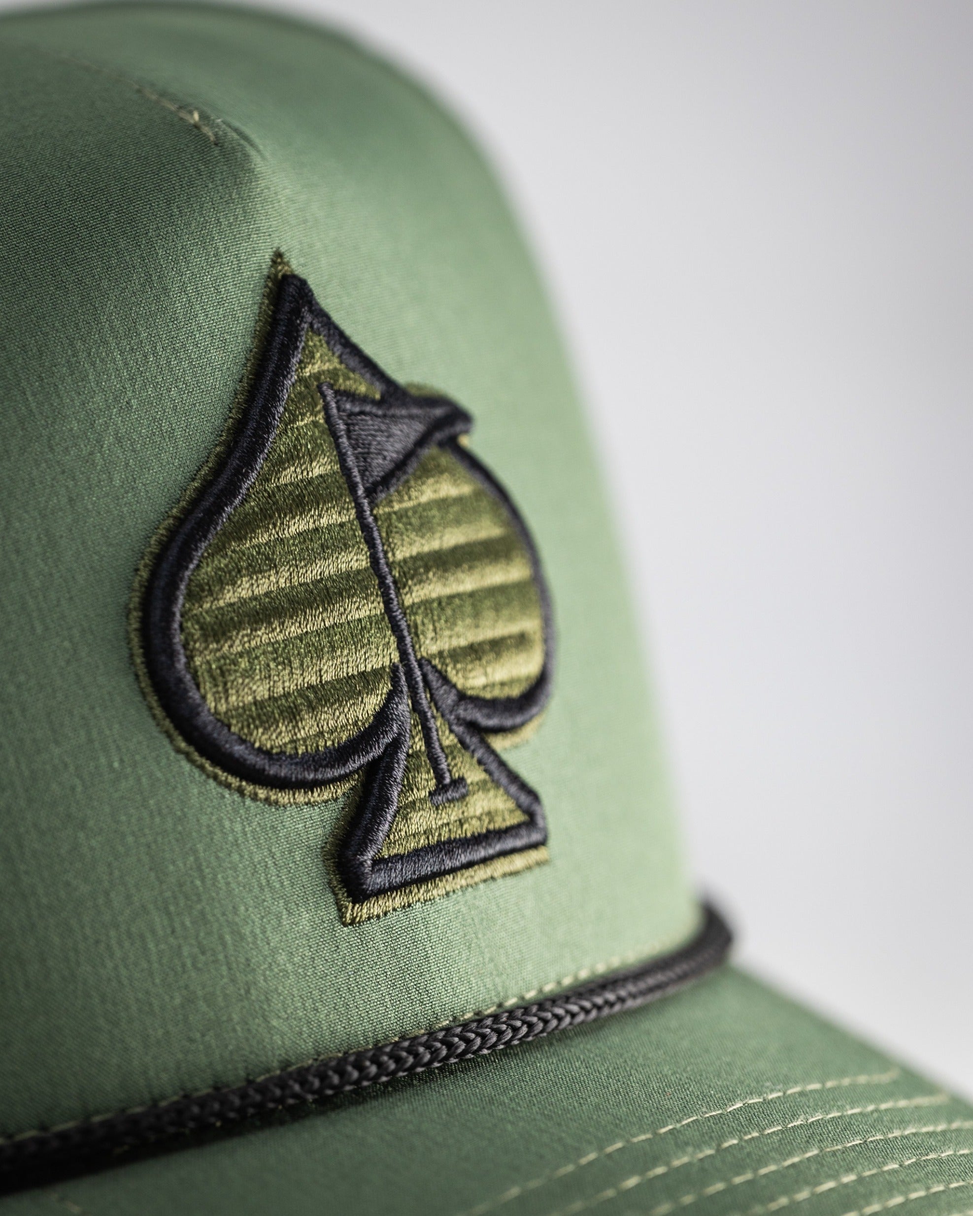 Olive perforated rope hat featuring a stylish spade logo, perfect for golfers seeking a bold accessory on the course.