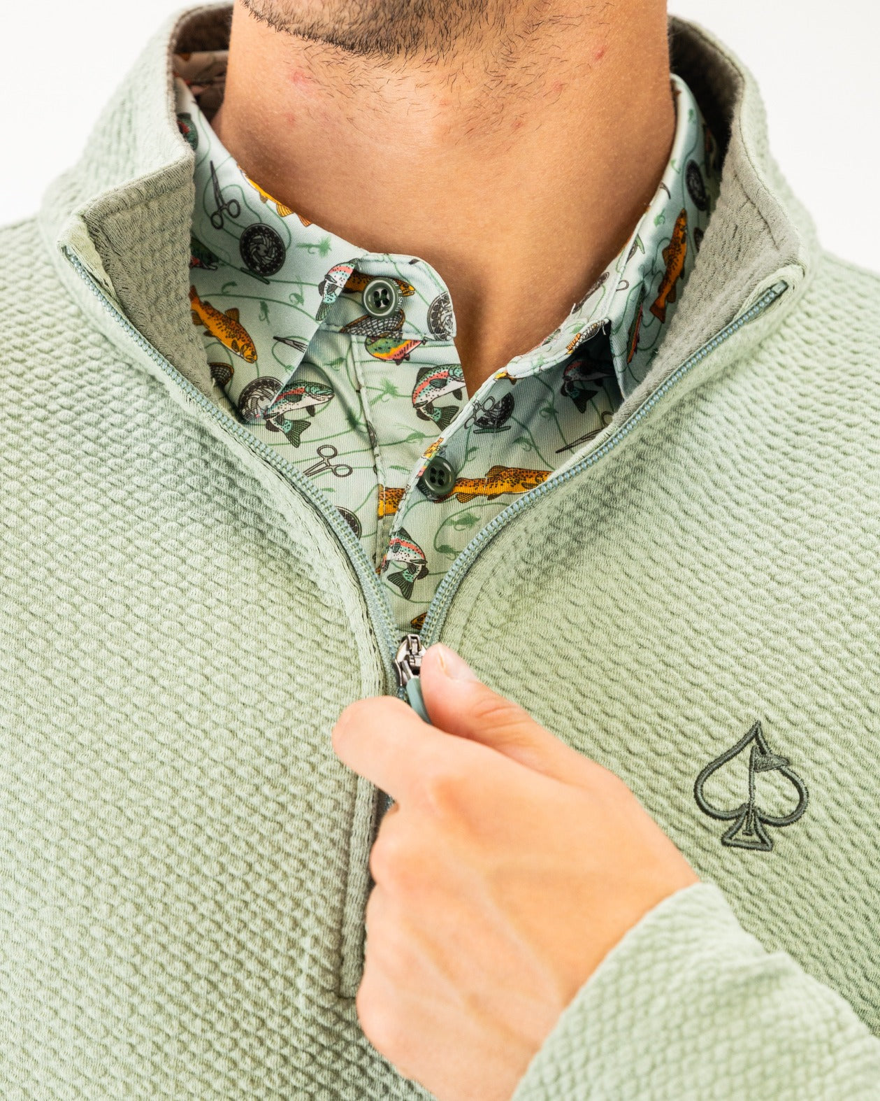 Olive waffle knit pullover with a half-zip collar, worn over a patterned shirt featuring golf-themed designs.