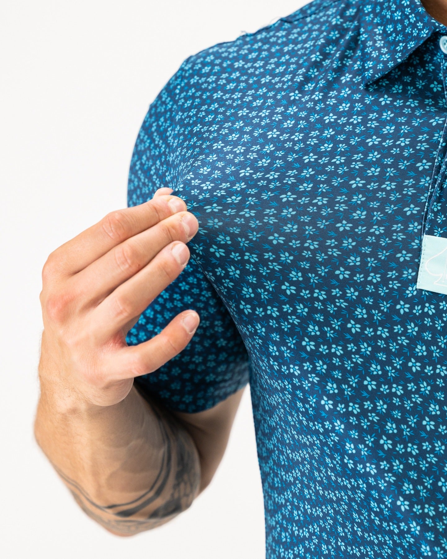 Men's blue polo shirt featuring a micro floral pattern, showcasing a close-up of the fabric and collar.