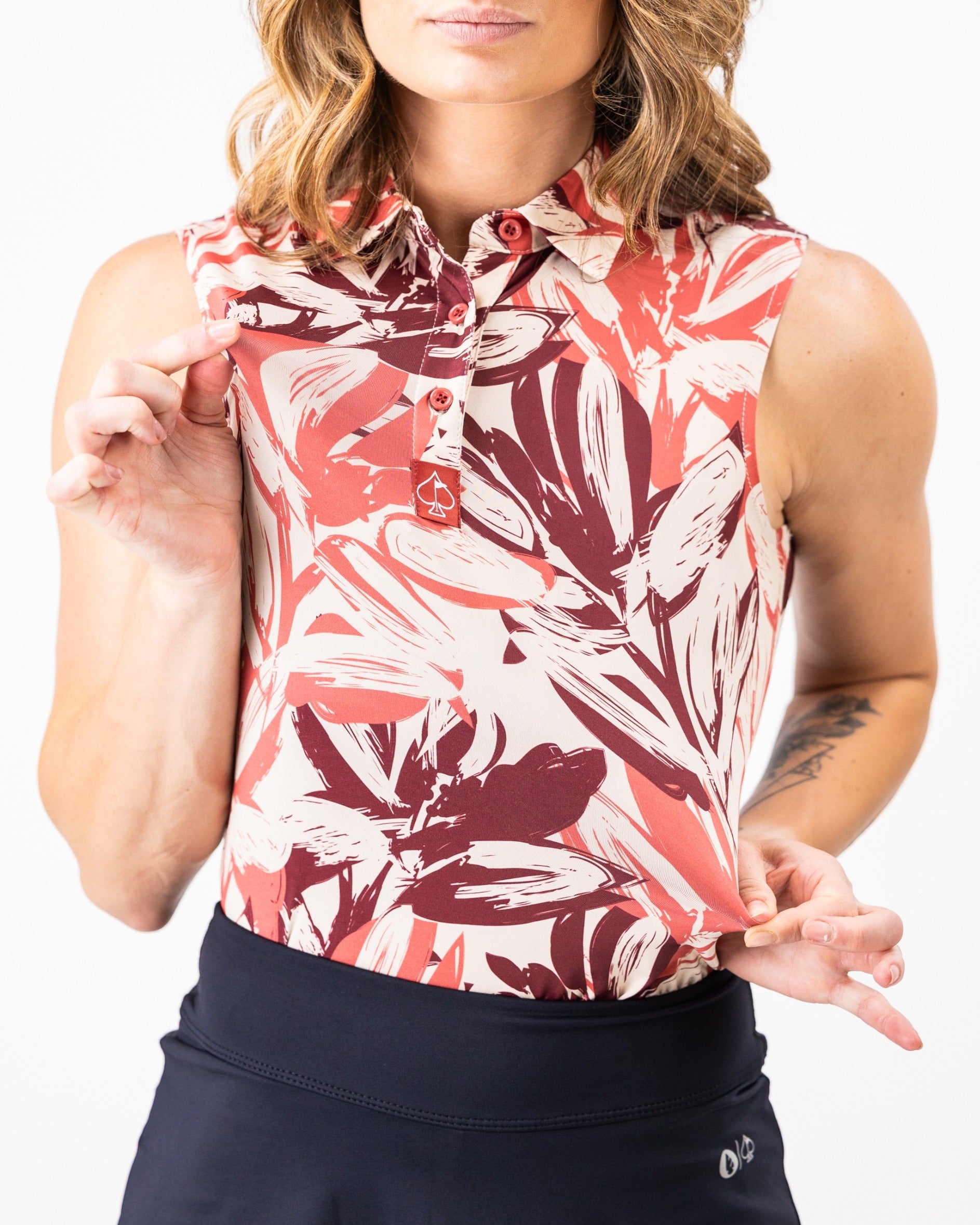 Stylish women's sleeveless golf top featuring a vibrant brushed floral pattern in warm tones, paired with a sleek black skirt.