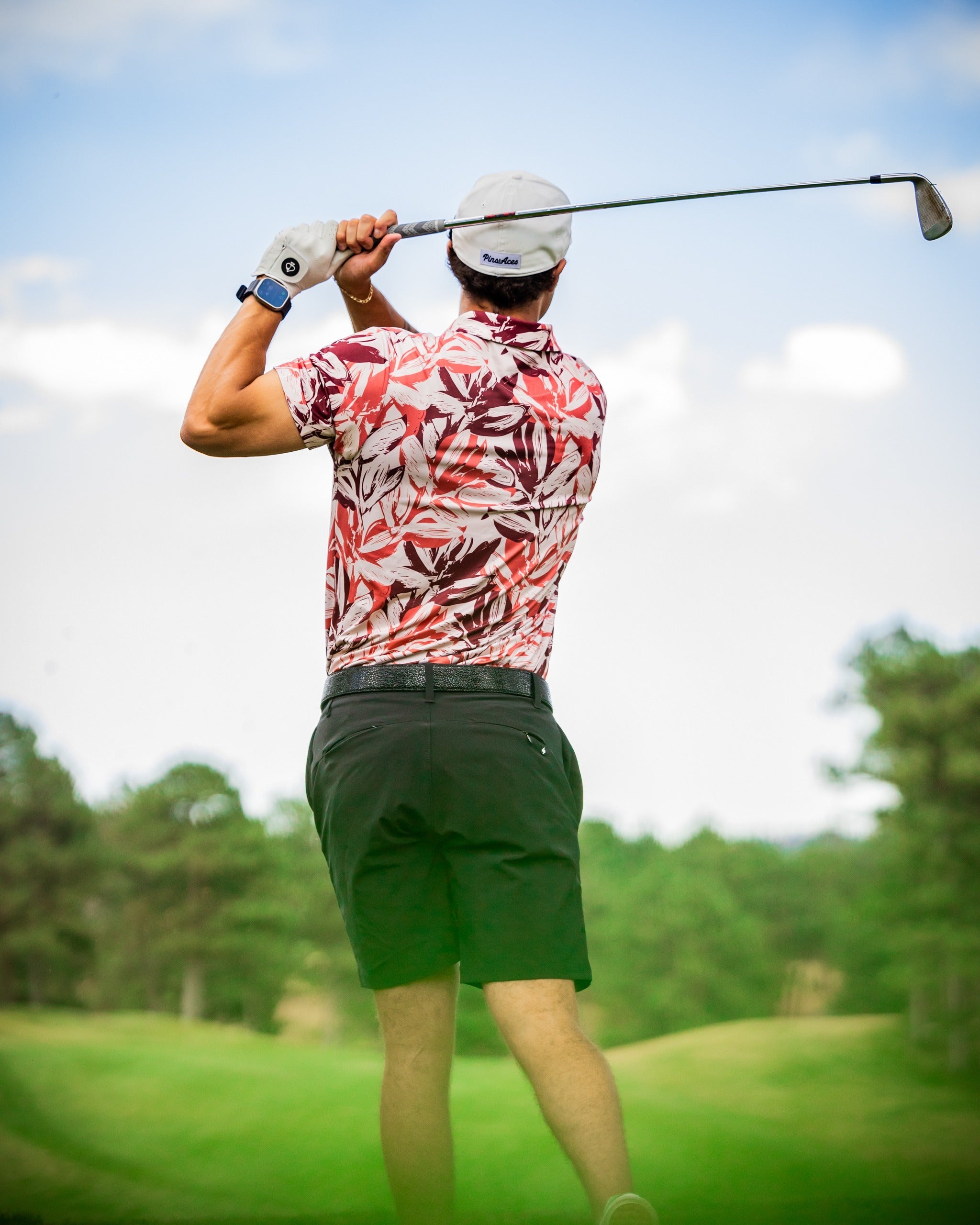 A golfer swings a club wearing a brushed floral polo shirt, showcasing a vibrant floral pattern against a green landscape.