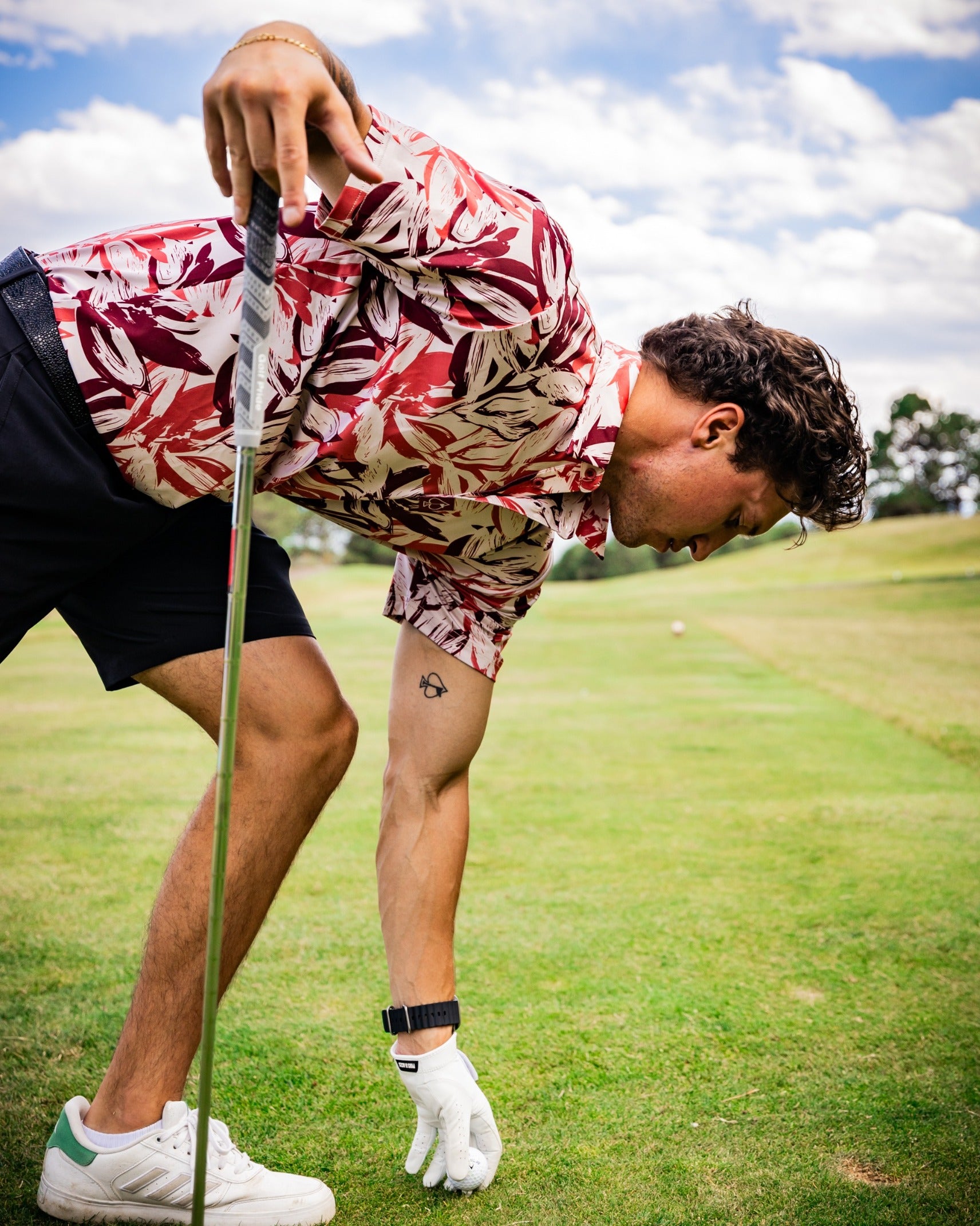 A golfer in a brushed floral shirt and shorts prepares to take a shot on the course, showcasing bold style and confidence.