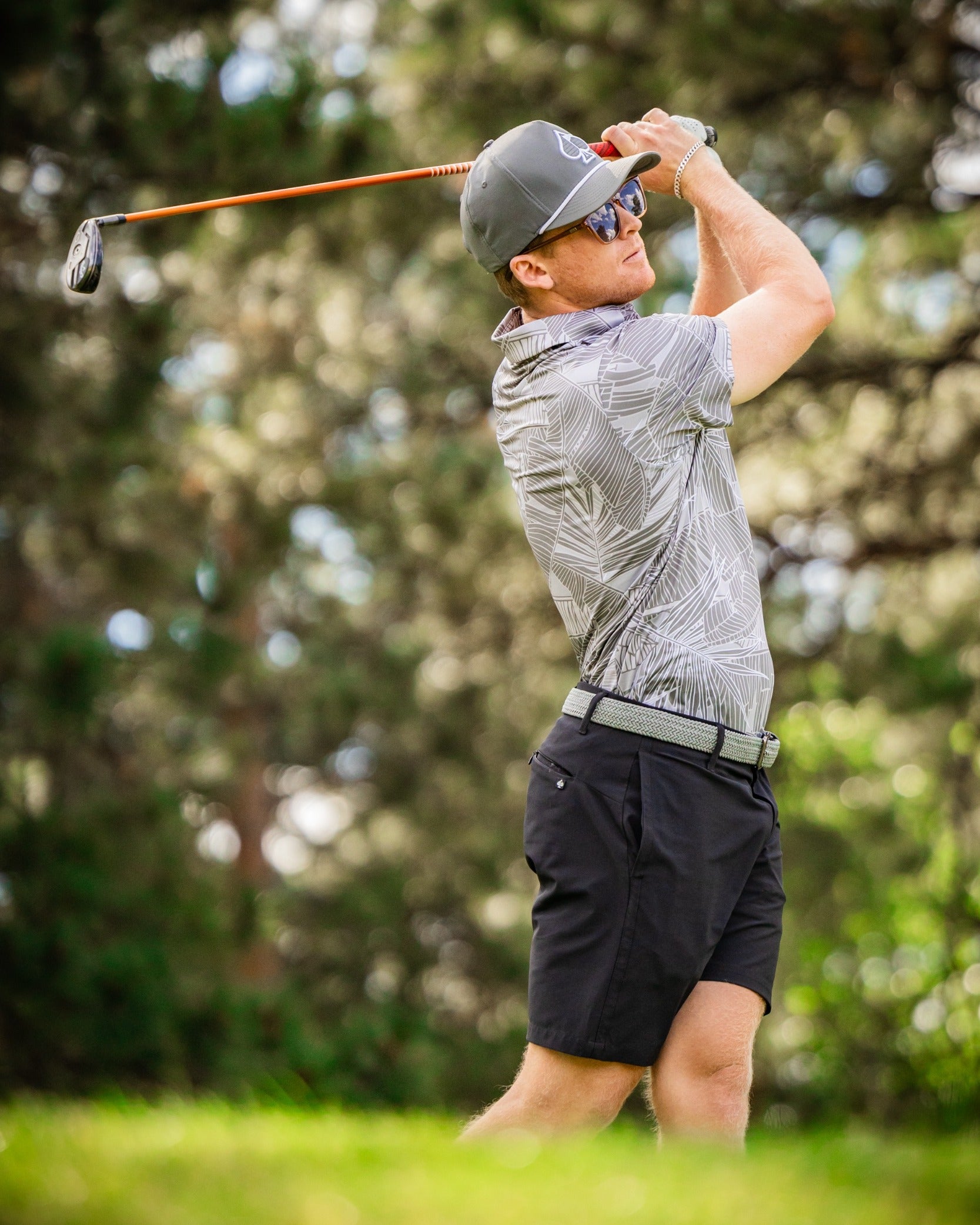 A golfer swings a club on the course, wearing a stylish palm-patterned shirt and shorts, showcasing bold golf fashion.