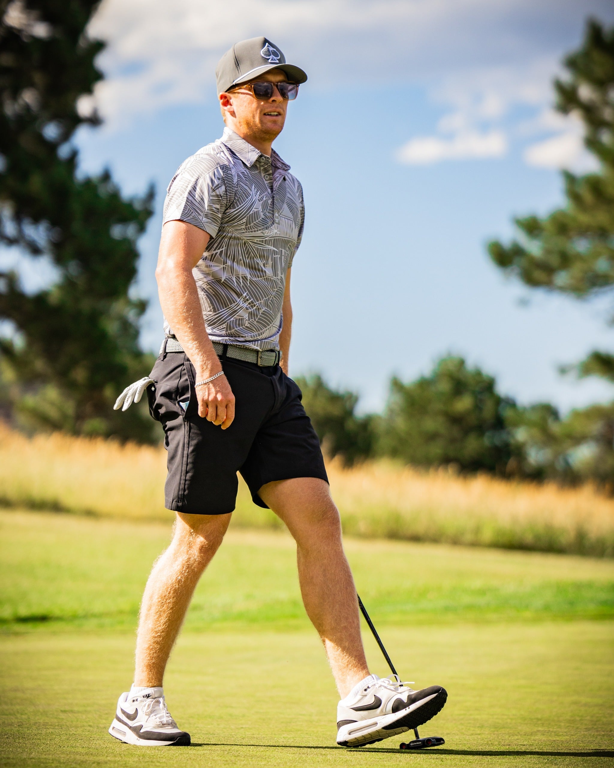 A golfer walks confidently on the course wearing a stylish palm-patterned polo shirt and shorts, showcasing bold golf fashion.