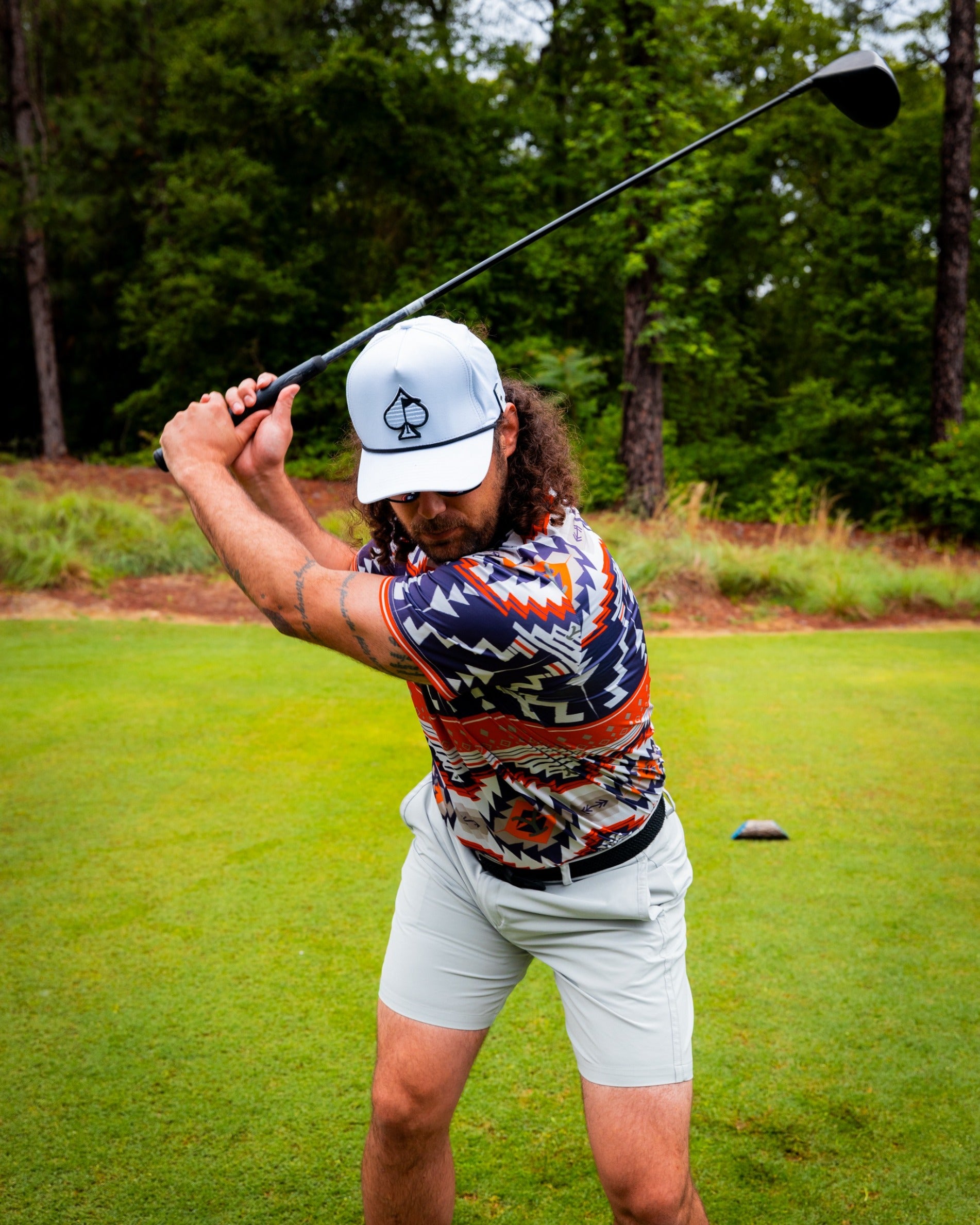 A golfer swings a club on the course, wearing a colorful patterned shirt and a light cap, showcasing a bold style.