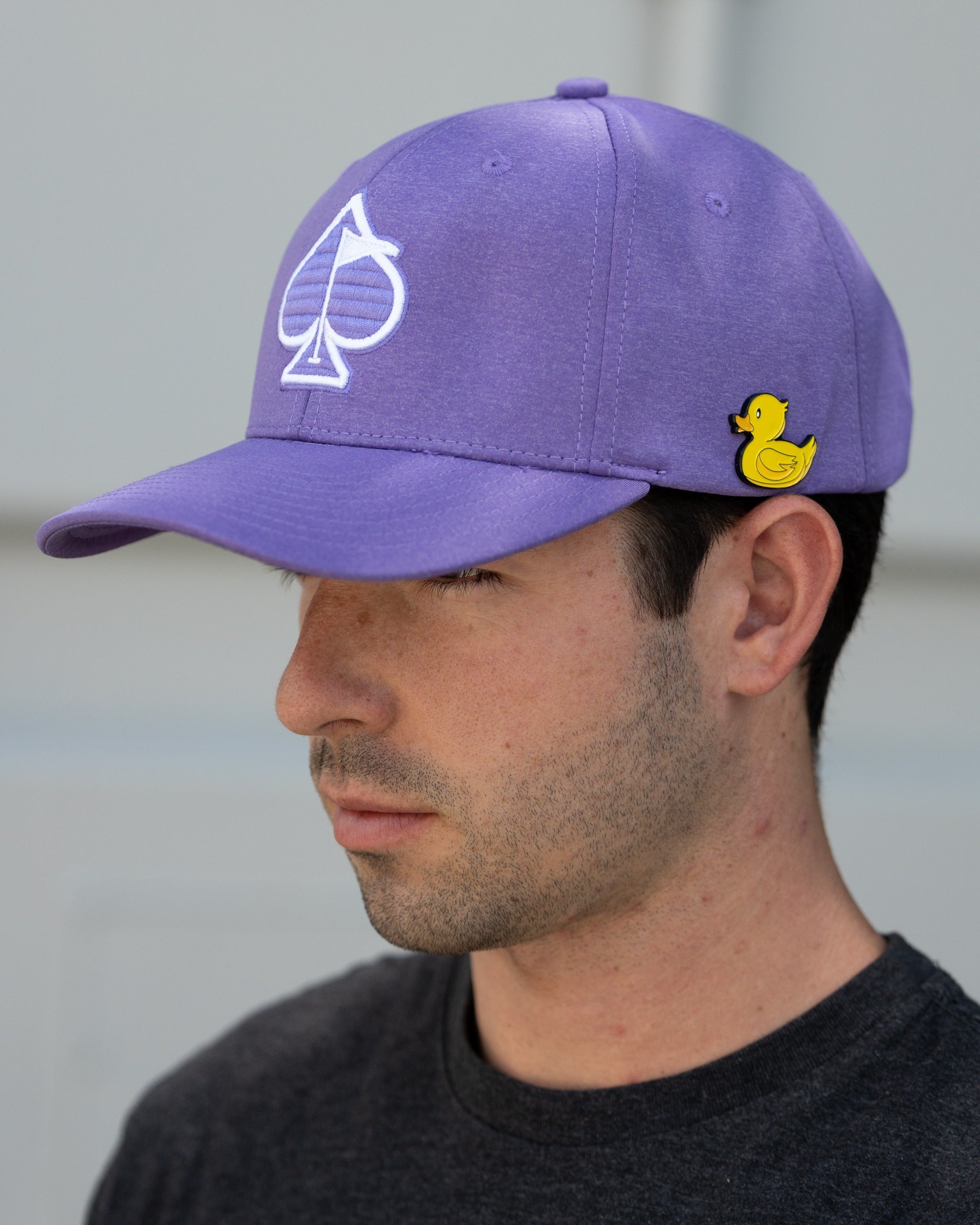Lavender Performance Spade Hat featuring a white spade logo and a playful yellow duck pin, worn by a man.