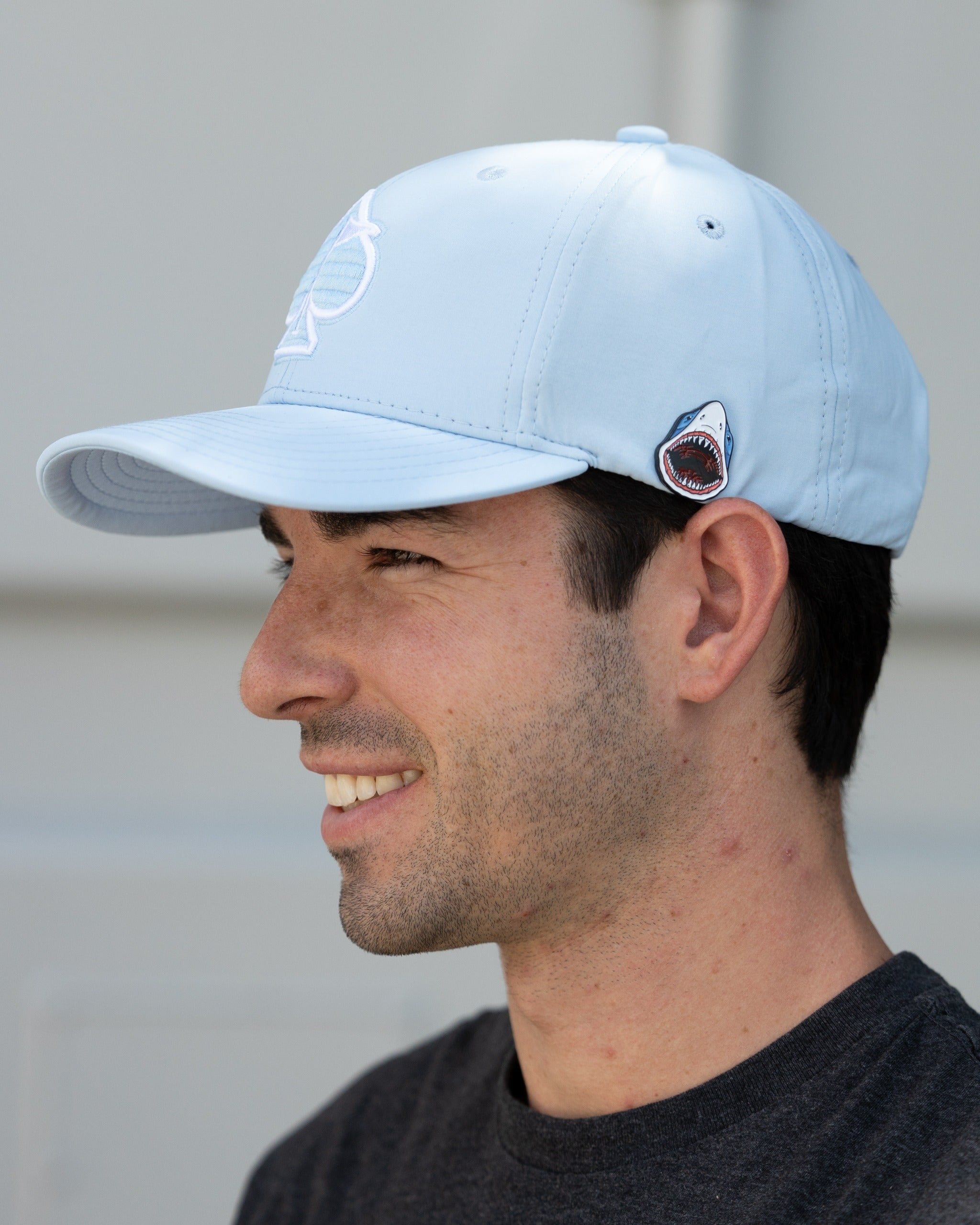 Carolina blue performance hat featuring a spade logo and shark emblem, modeled by a smiling man.