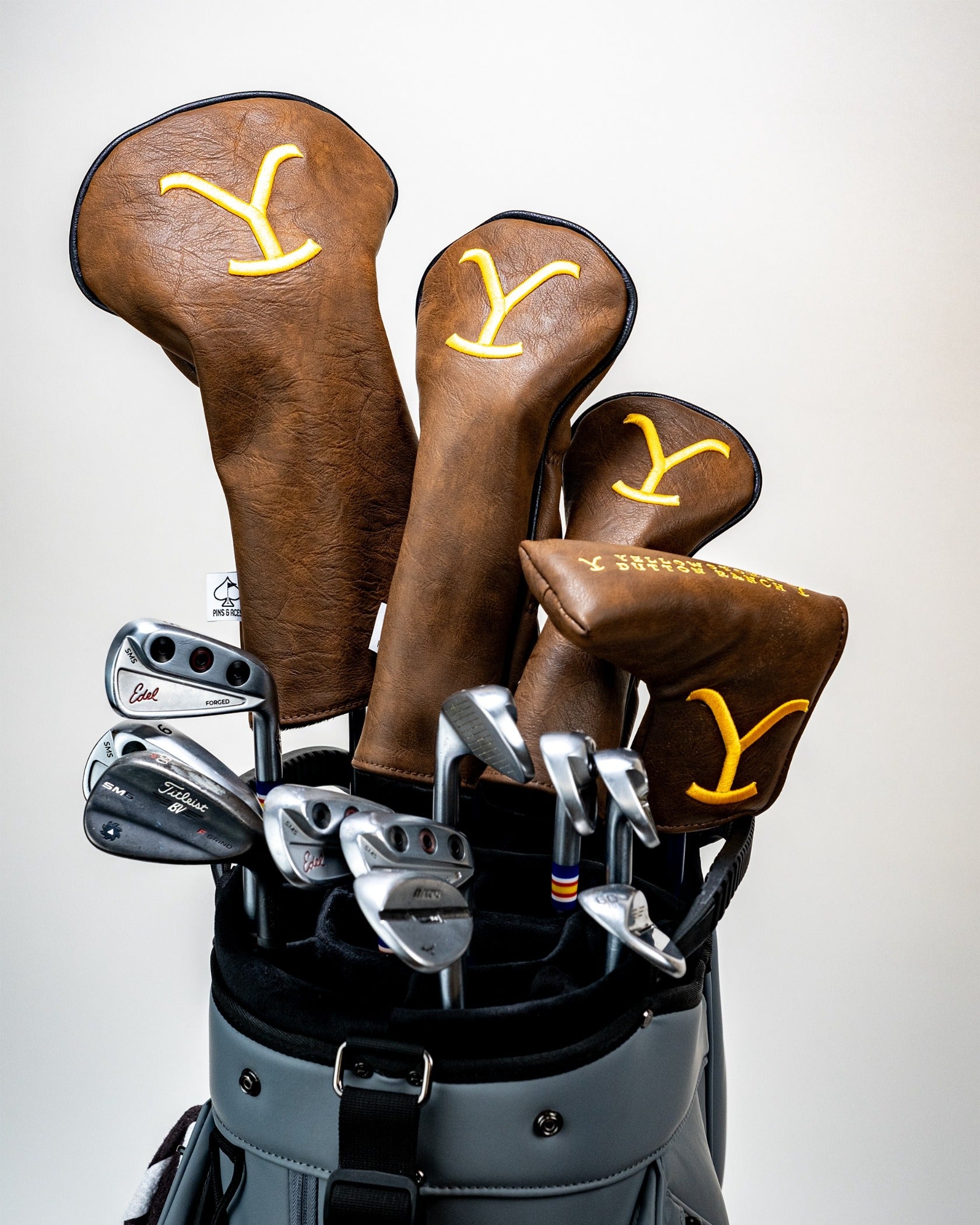 Yellowstone blade putter cover in rich brown leather, featuring a bold yellow logo, paired with matching headcovers in a golf bag.