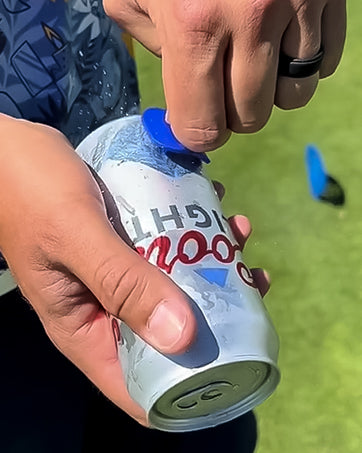 A golfer using The Shottee Golf Tee to easily open a beverage can on the course, showcasing its practical design.