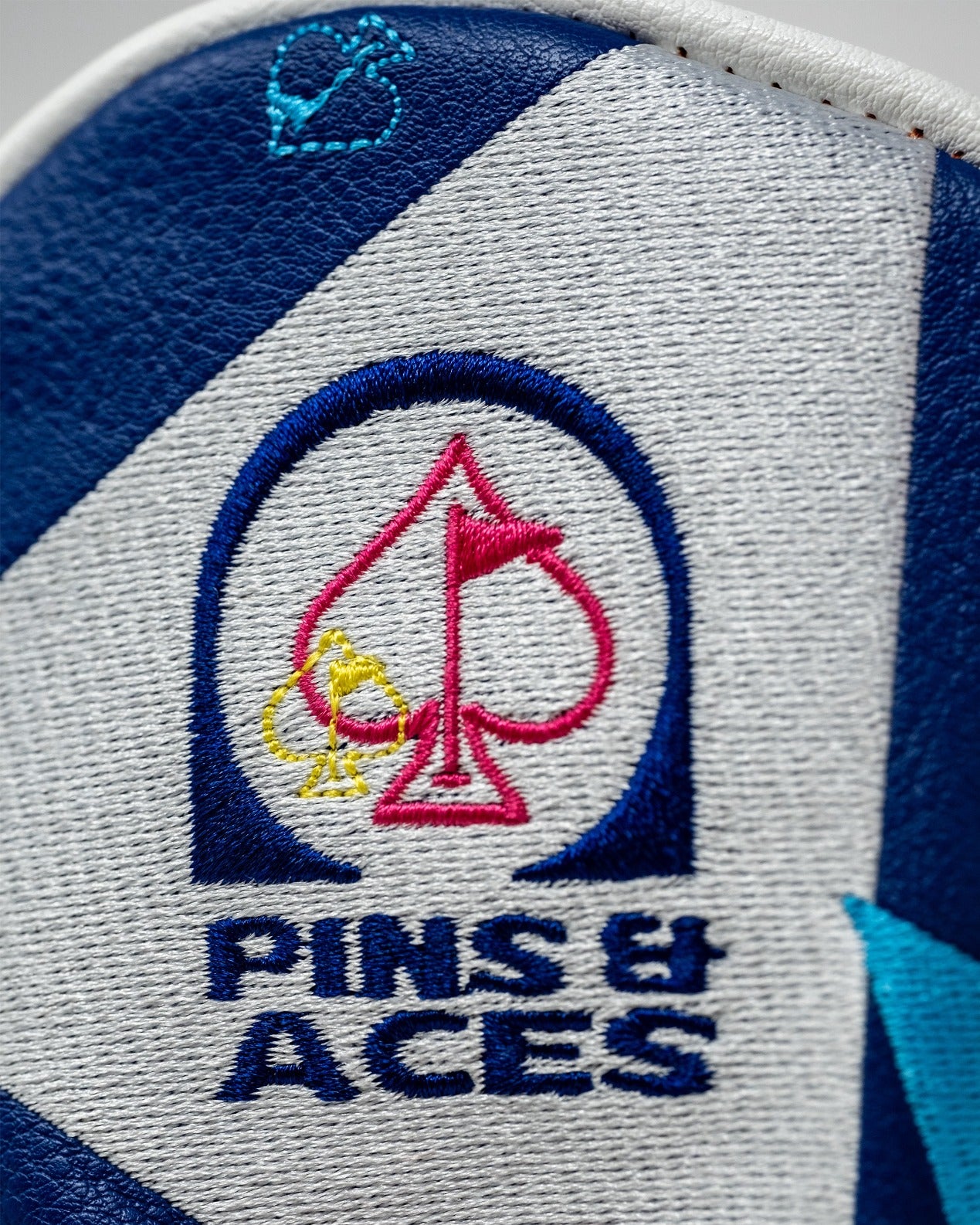 Close-up of the Pins and Aces Mild Sauce Hybrid Cover featuring a colorful logo with spade and bird designs.