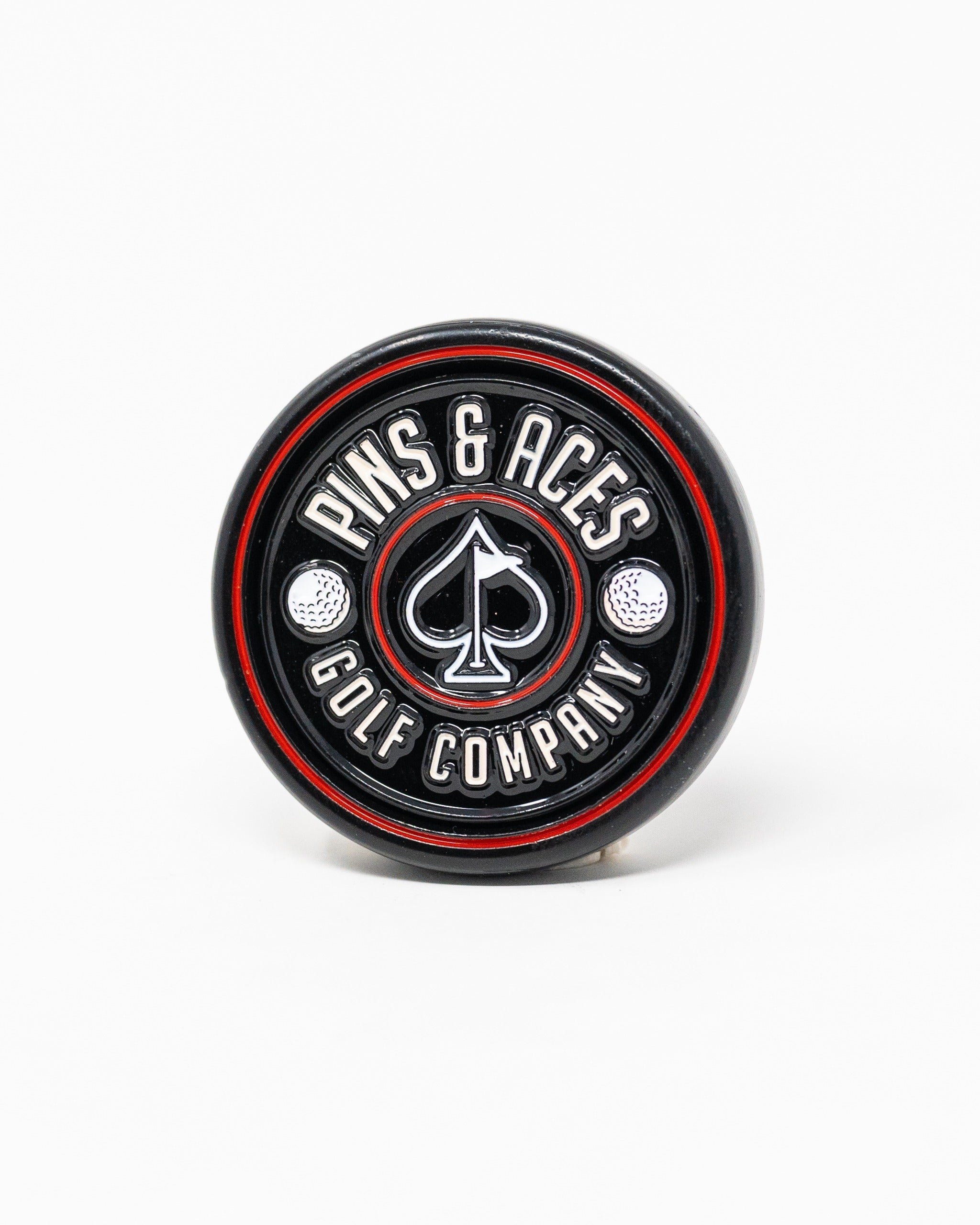 Black pop-out medallion ball marker featuring the Pins and Aces logo with a spade design and golf ball accents.