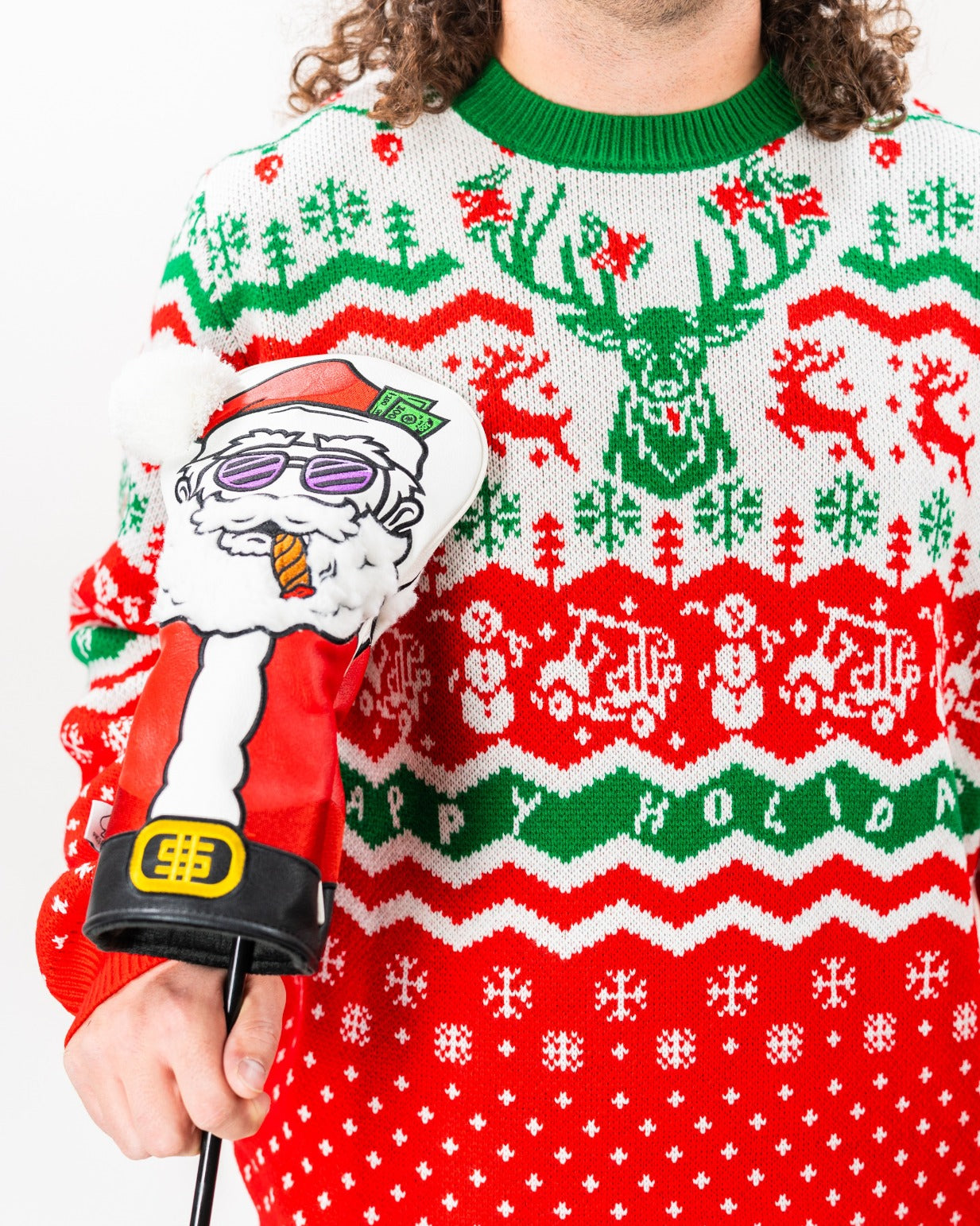 A person wearing a festive red and green ugly sweater featuring holiday patterns, holding a Santa-themed golf headcover.