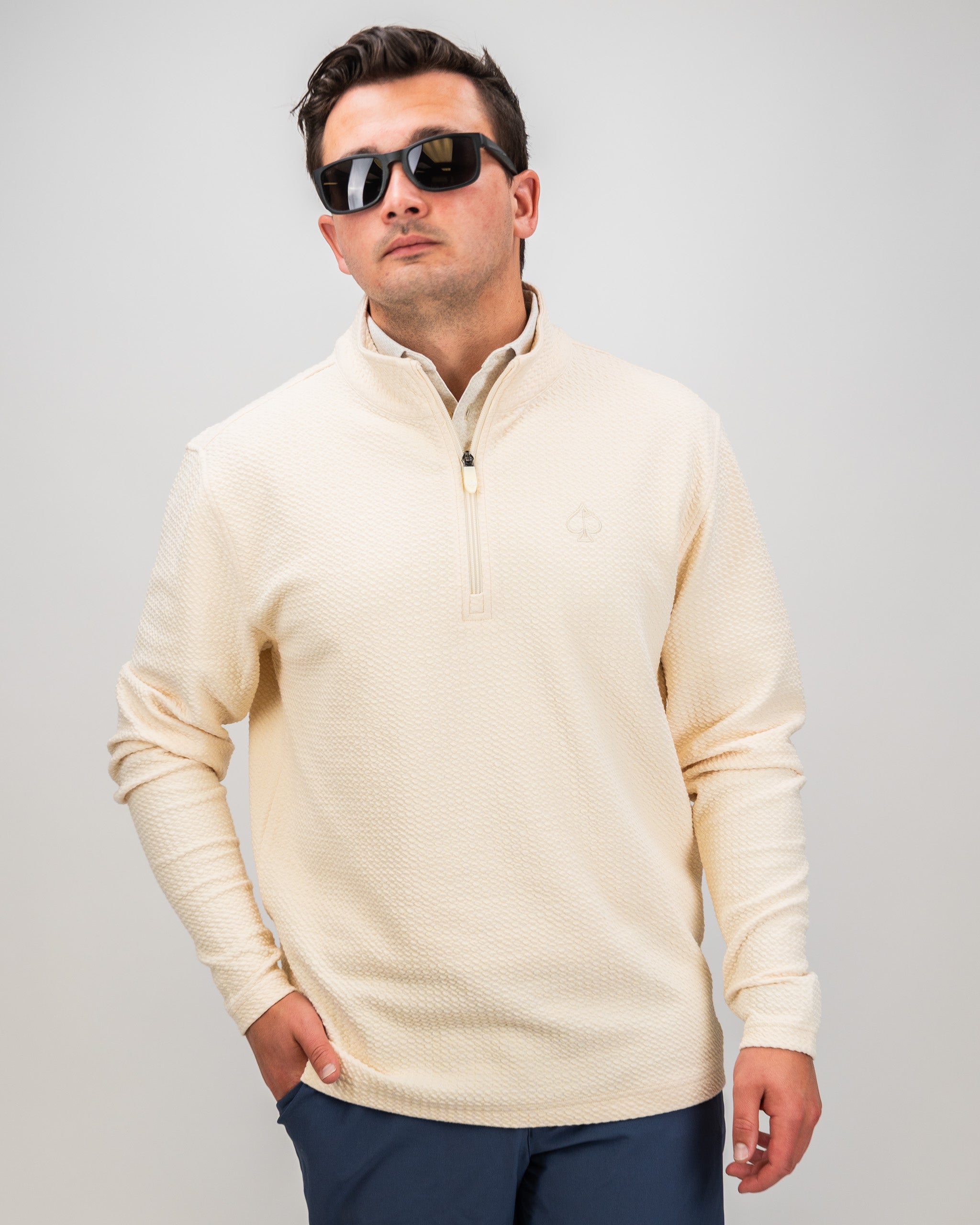 Cream waffle knit pullover with a half-zip collar, featuring a subtle logo, worn by a man in sunglasses.