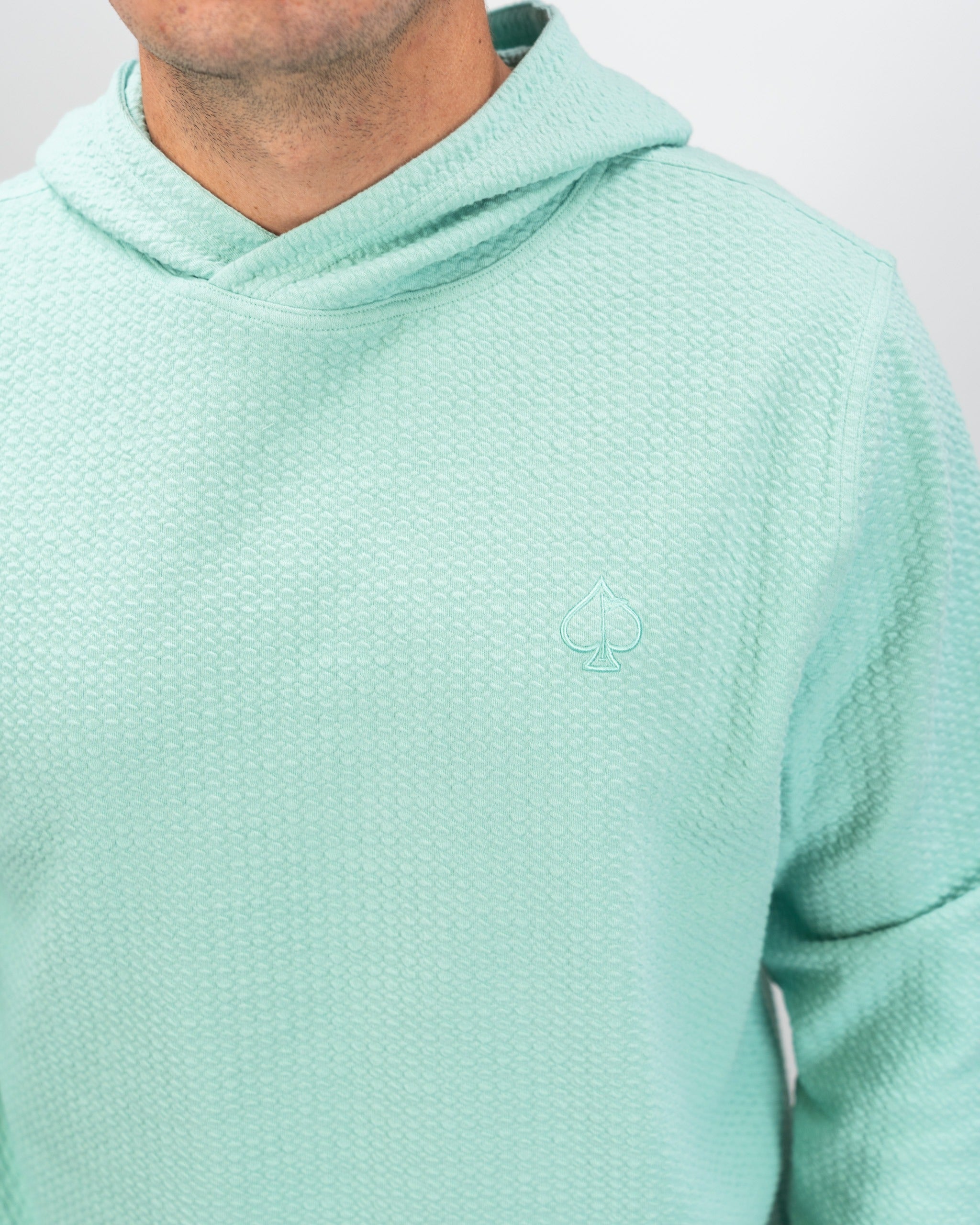 Bright mint waffle knit hoodie featuring a subtle spade logo, designed for comfort and style on the golf course.