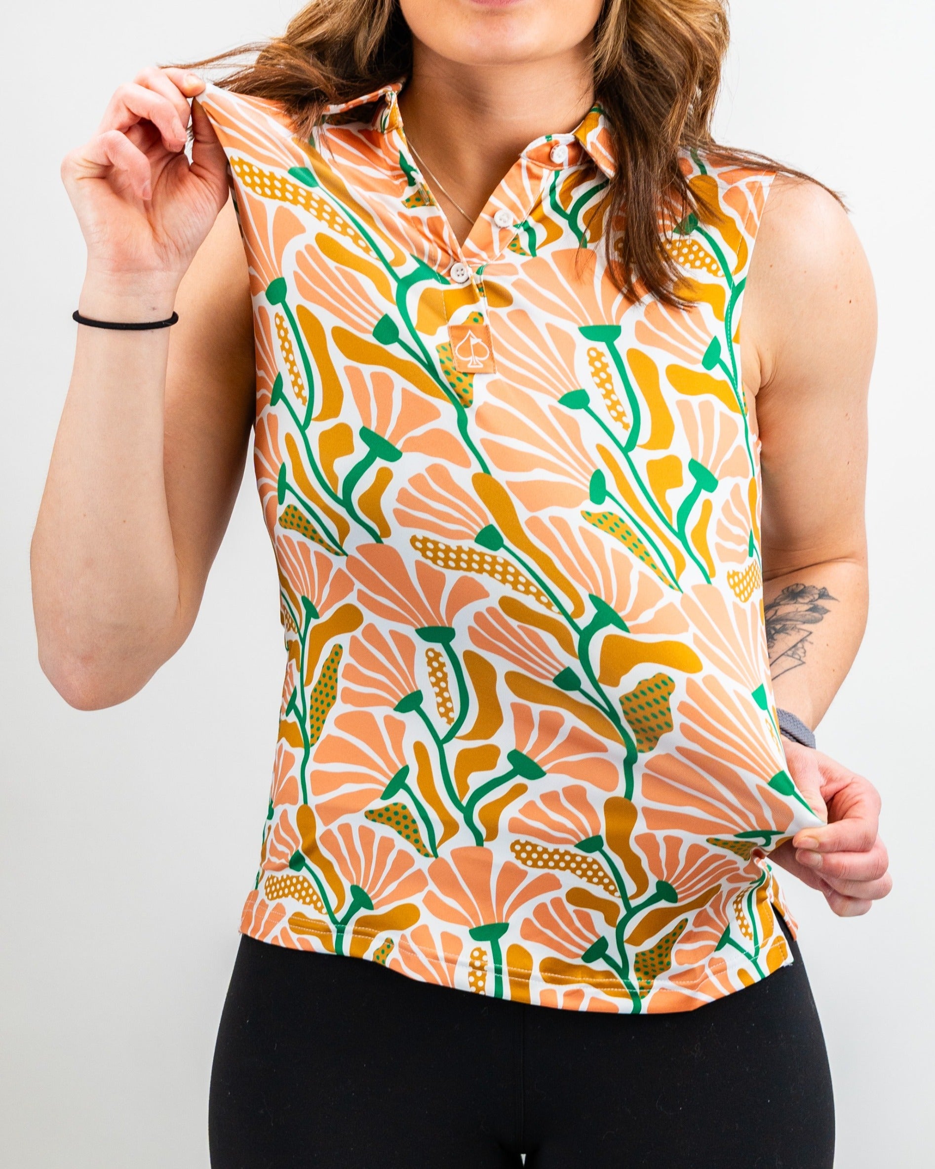 Brightly patterned women's sleeveless polo featuring floral designs in orange, green, and yellow, perfect for golf outings.