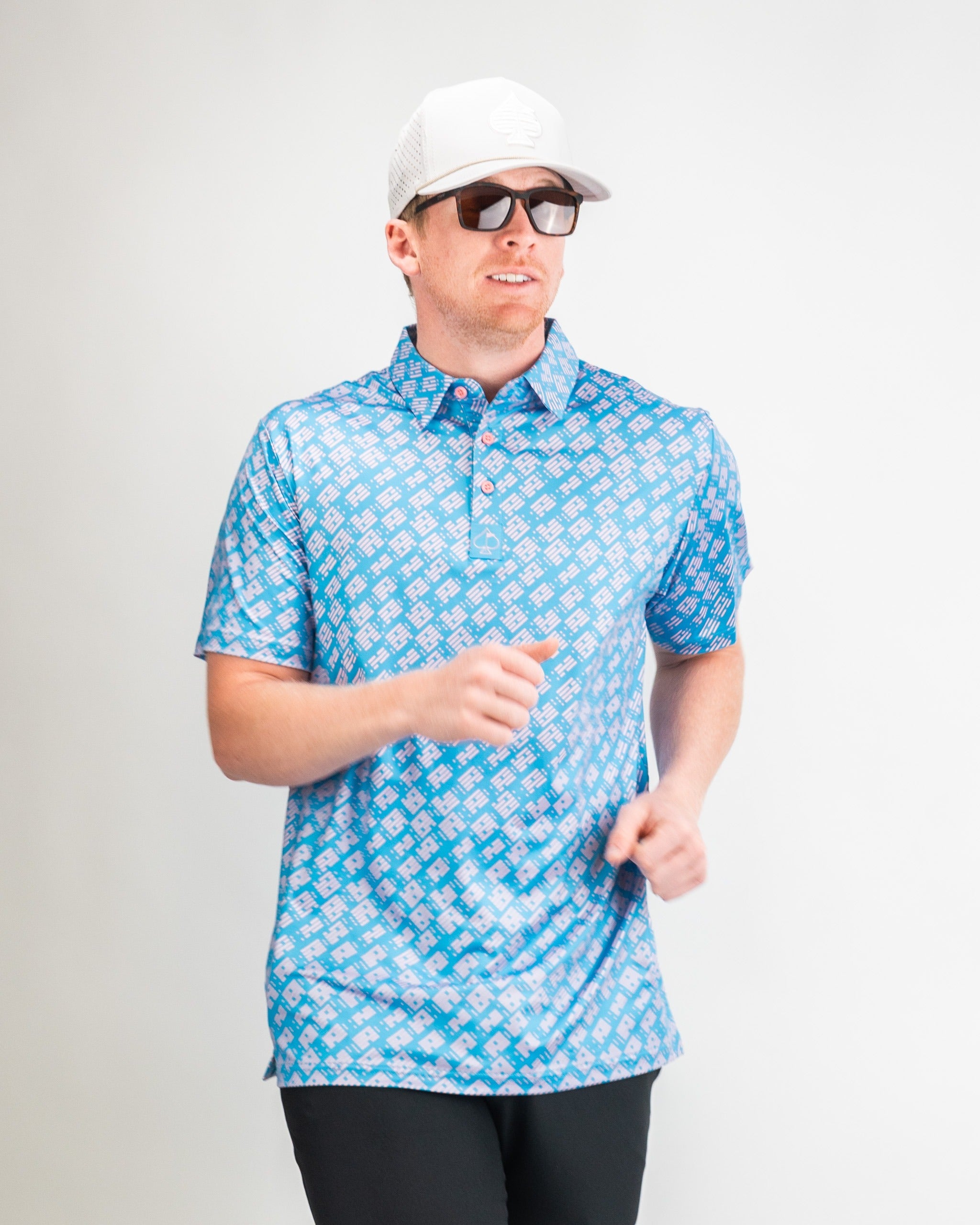 Man wearing a blue patterned golf polo shirt, sunglasses, and a white cap, showcasing a stylish athletic look.