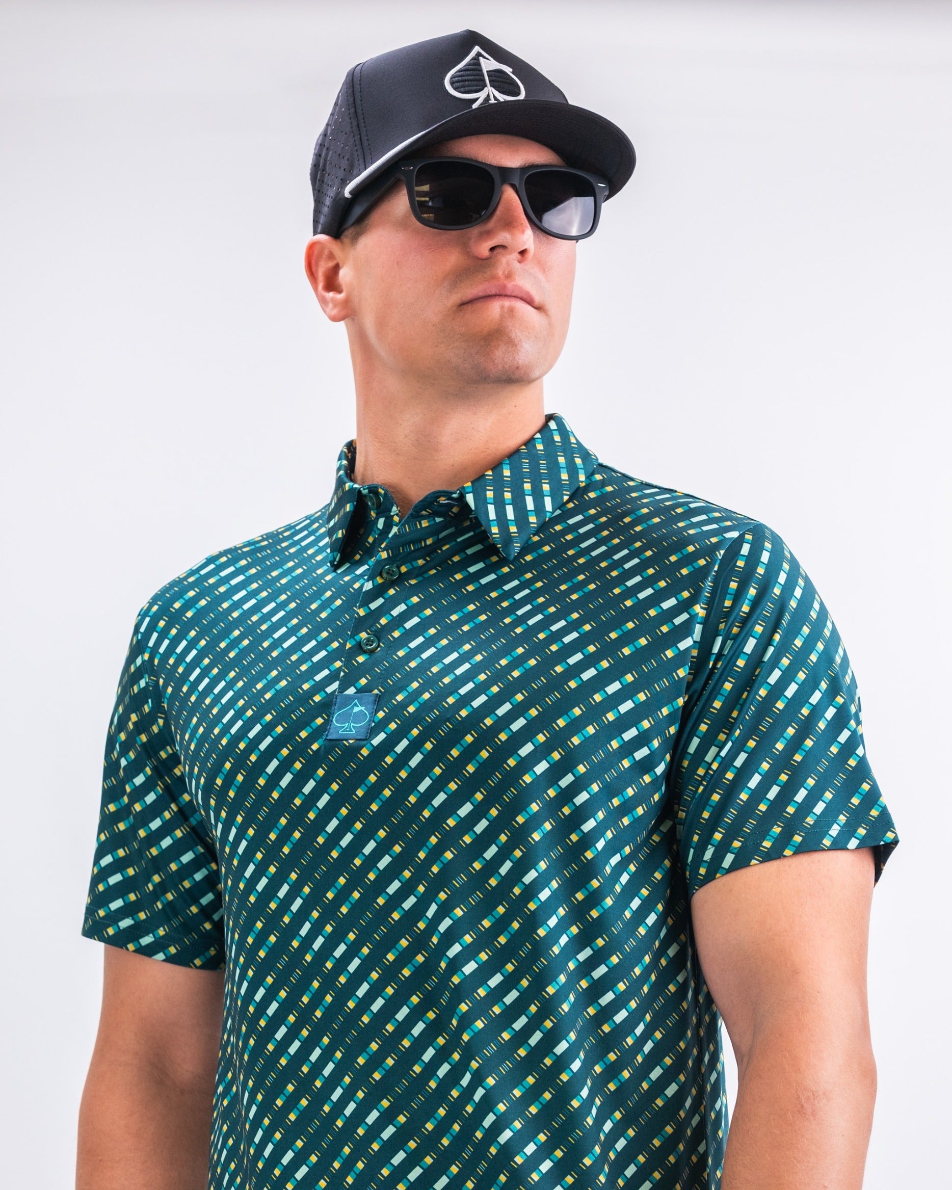 Stylish golfer wearing a green patterned polo shirt and black cap, showcasing bold golf apparel for a standout look.