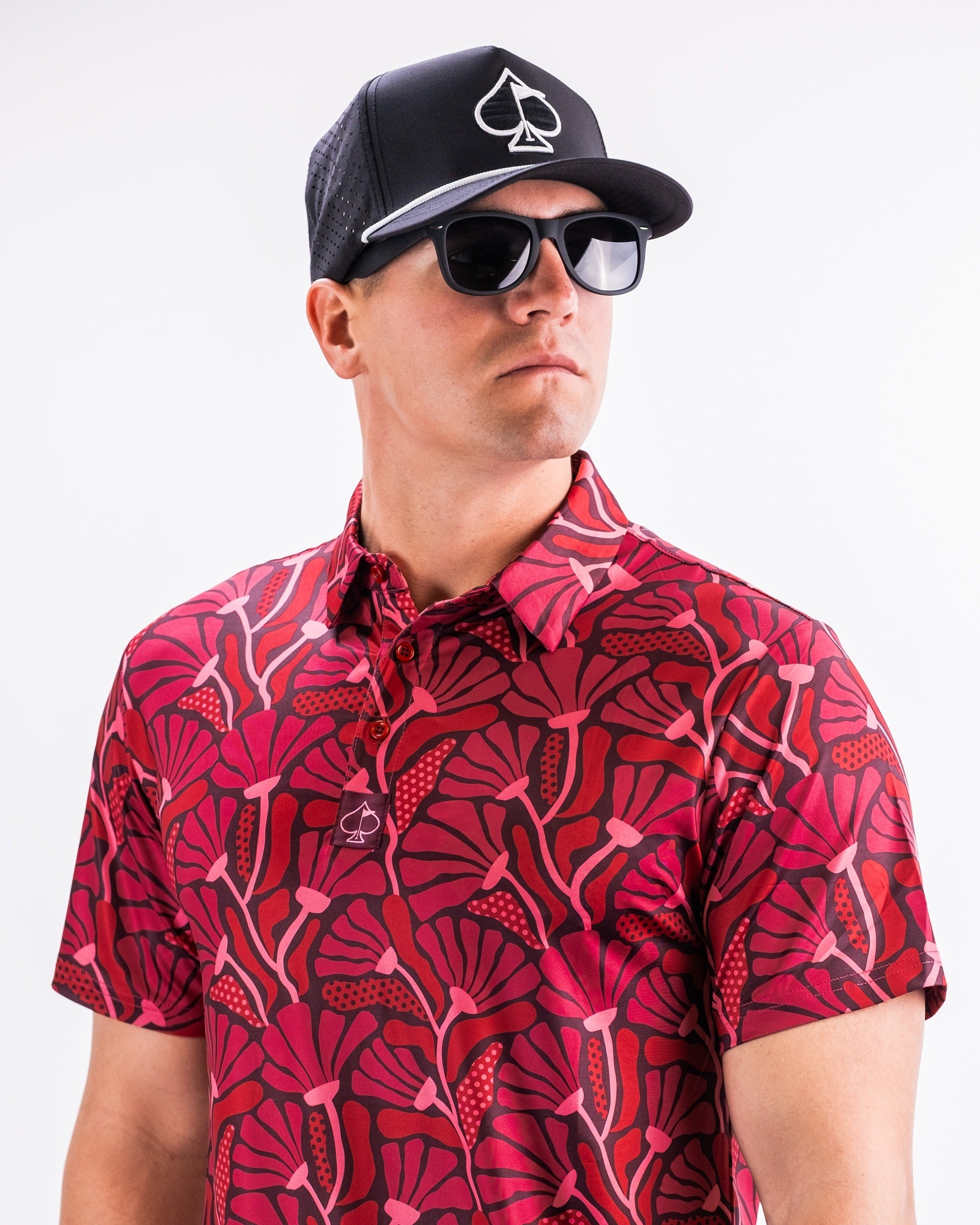 Bold crimson golf shirt featuring a vibrant floral pattern, paired with a black cap and sunglasses for a stylish look.