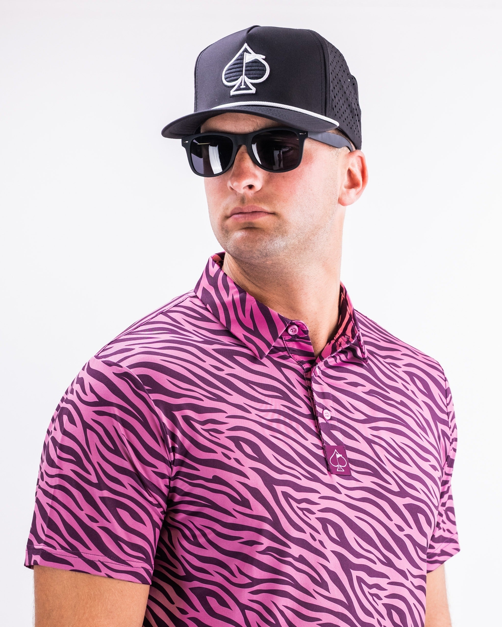 Man wearing a vibrant pink zebra print polo shirt and a black cap with a logo, styled with sunglasses for a bold golf look.