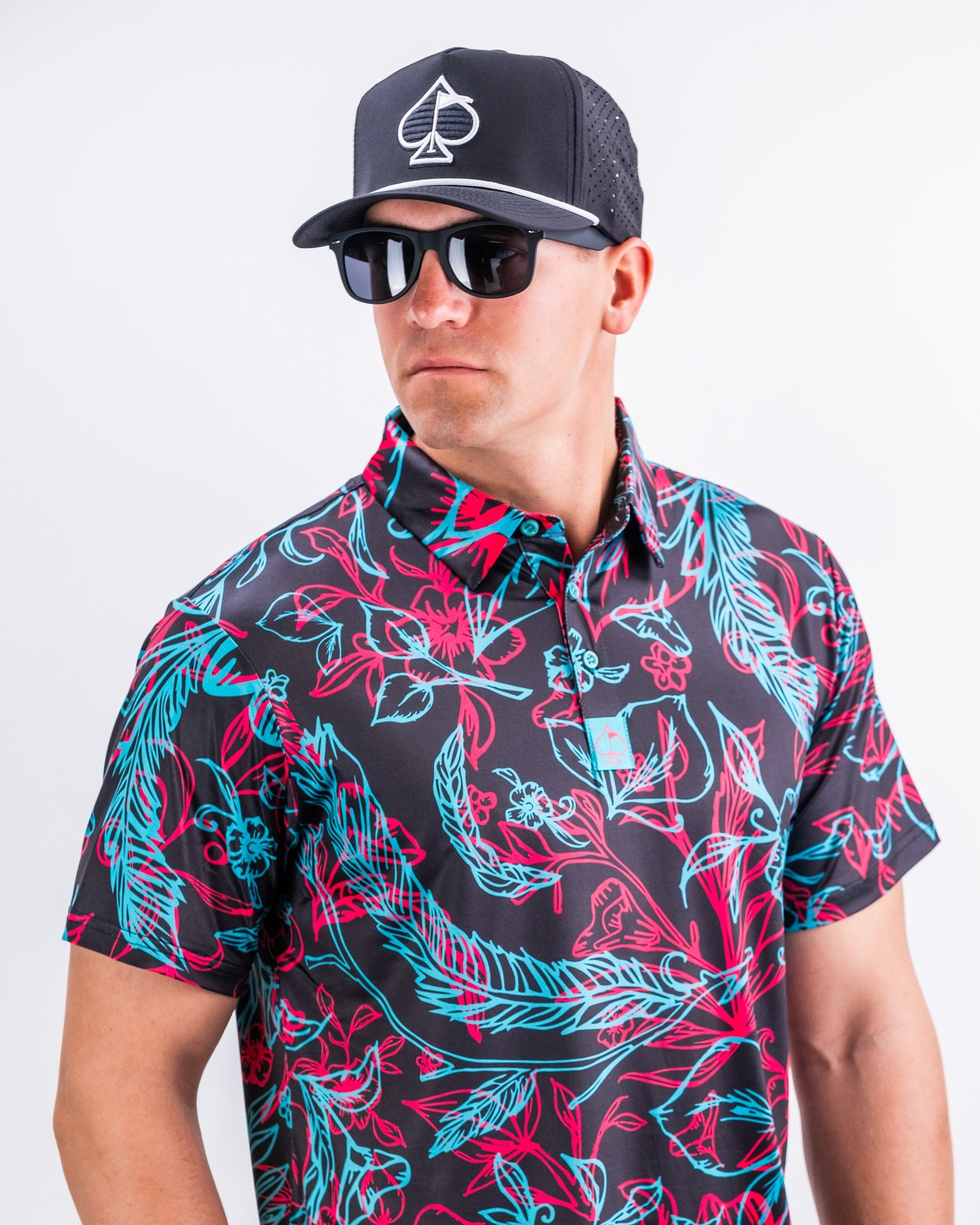 Bold floral print golf shirt in vibrant colors, worn by a man with sunglasses and a black cap, perfect for standout style on the course.