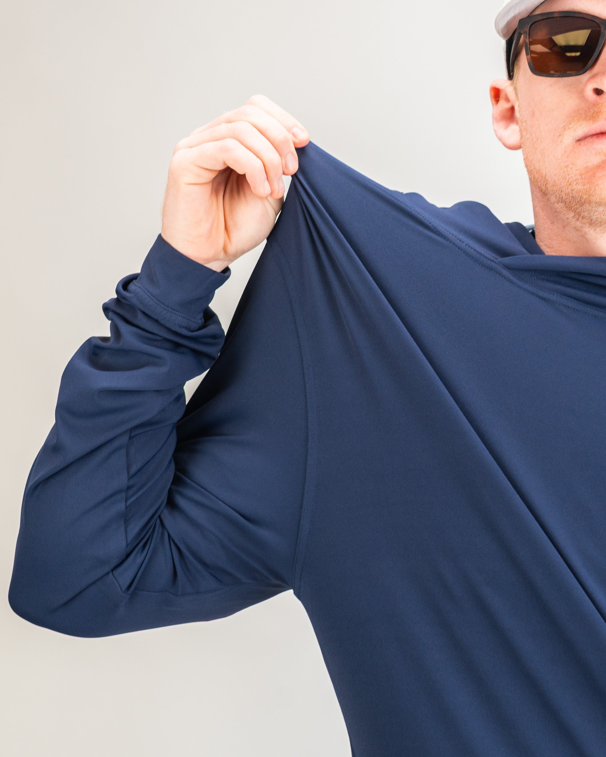 Navy performance golf hoodie being stretched by a golfer, showcasing its flexible and breathable fabric for comfort.