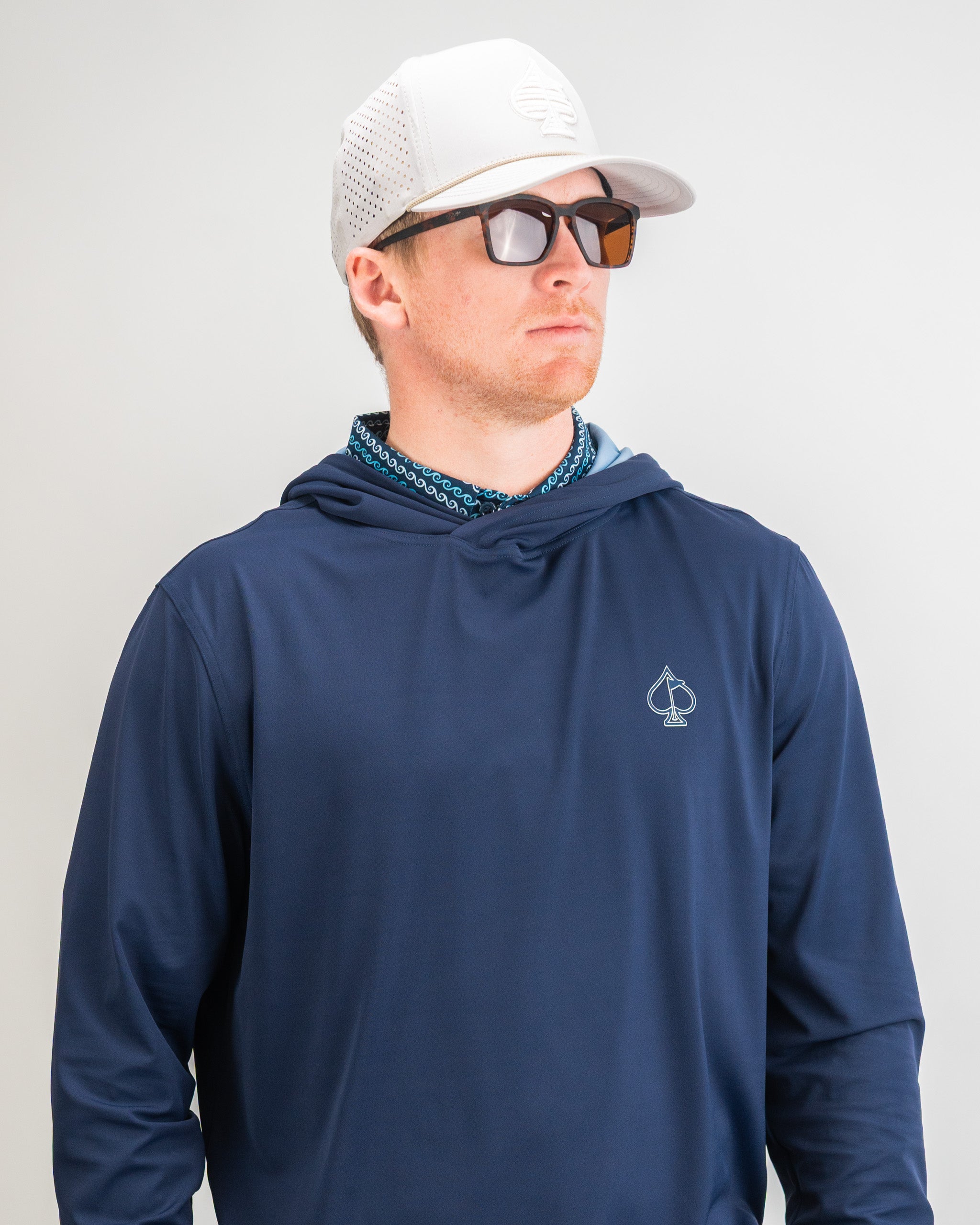 Navy performance golf hoodie featuring a logo, paired with sunglasses and a patterned shirt for a stylish look on the course.