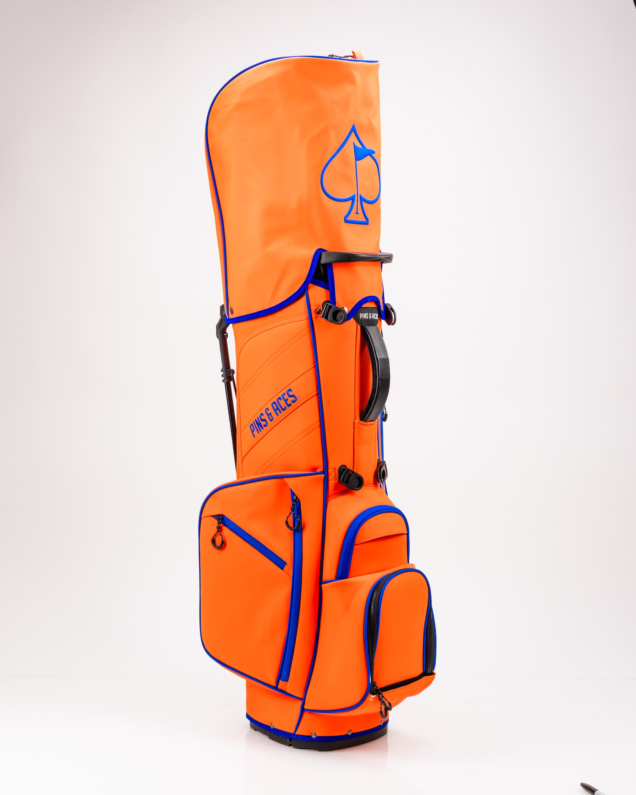 Bold orange golf bag with blue accents and spade logo, featuring multiple pockets for accessories and clubs.