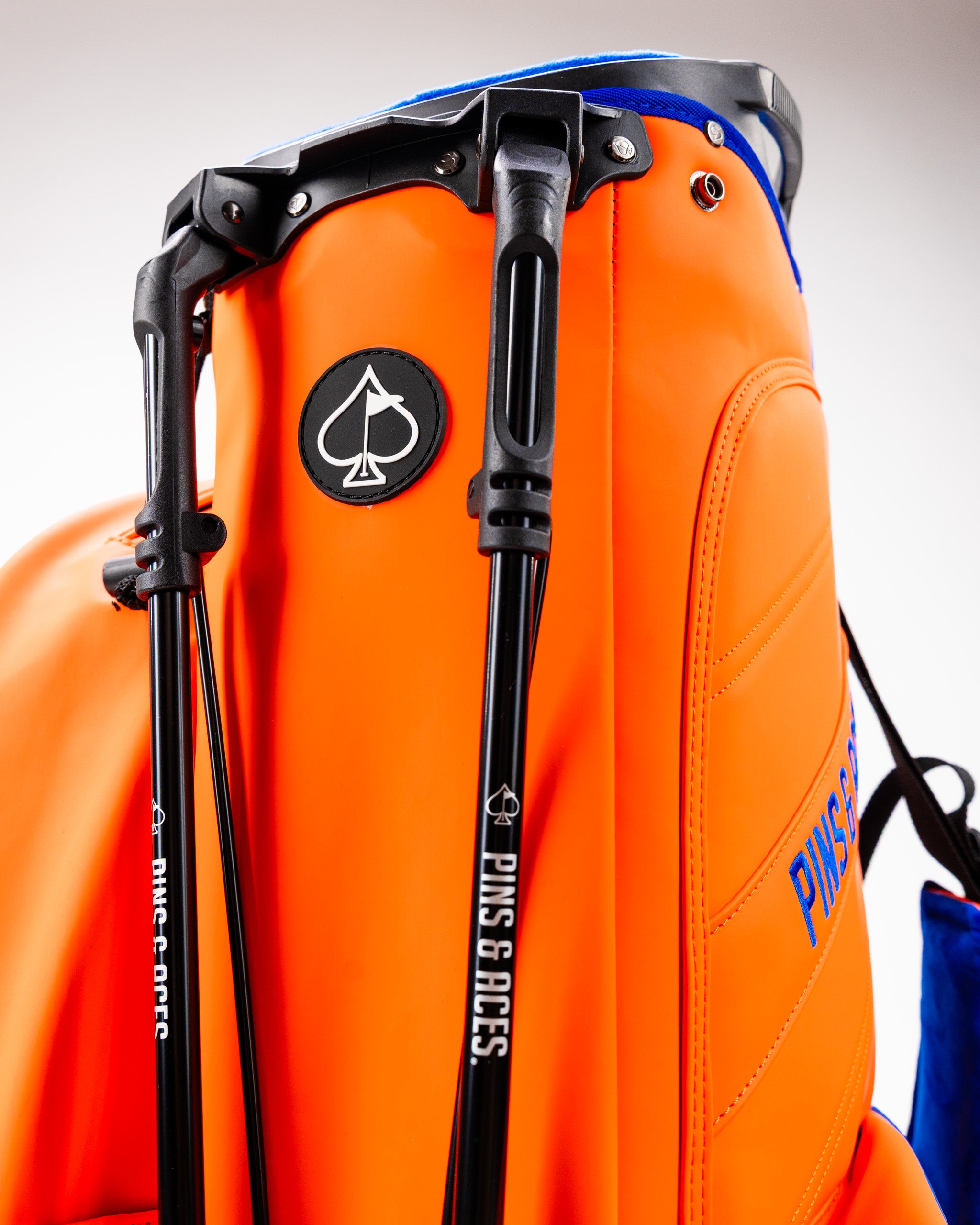 Bold orange golf bag featuring a sleek design, adjustable straps, and the Pins and Aces logo for standout style on the course.