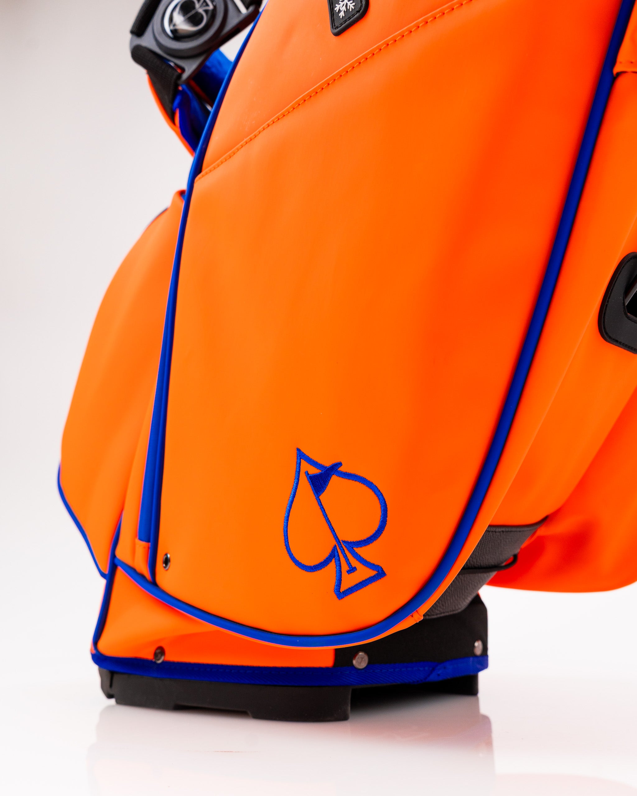 Bright orange golf bag featuring a blue spade logo, designed for style and functionality on the golf course.