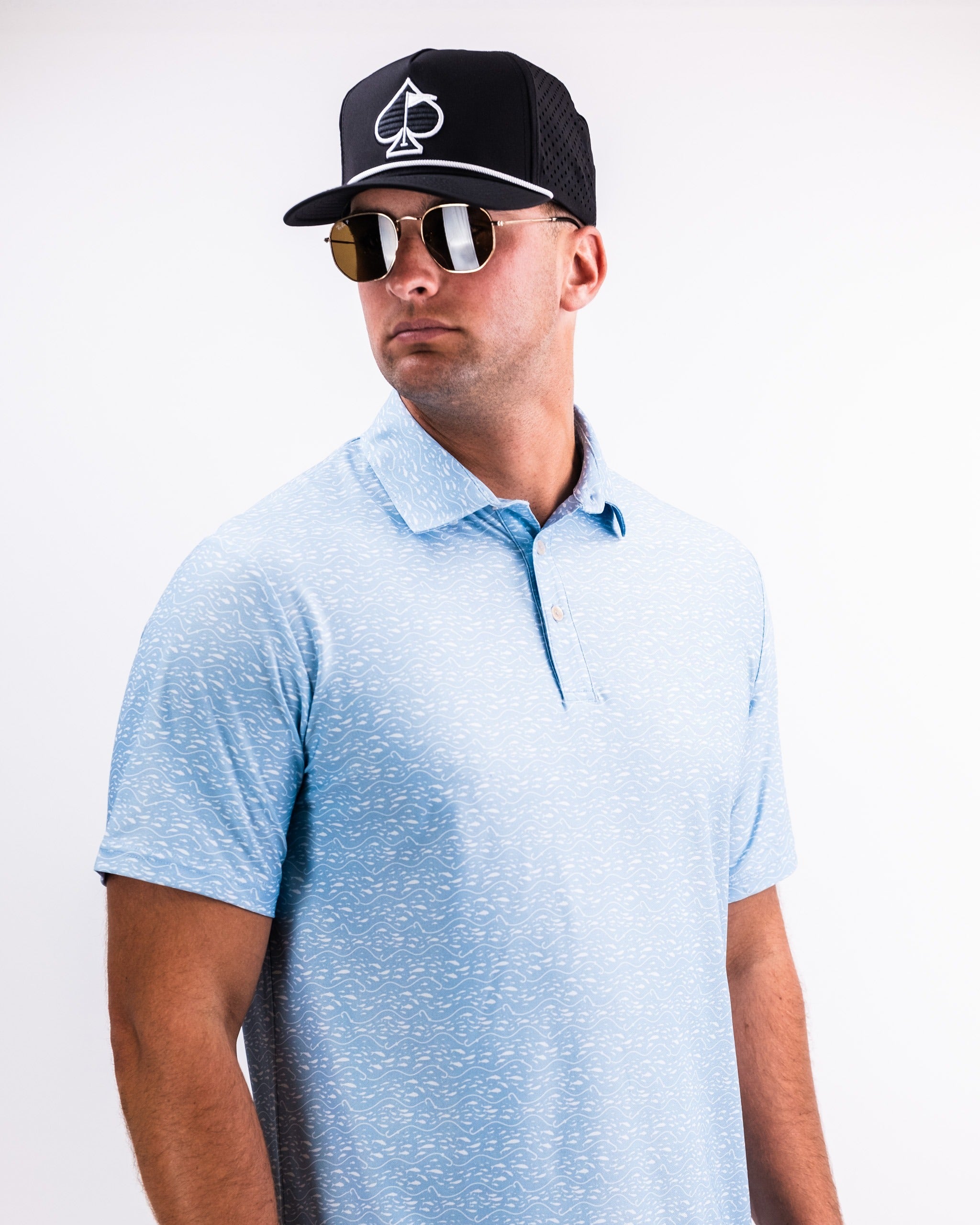 Player Preferred Polo in Tidal Flow features a light blue pattern, paired with a black cap and sunglasses for a stylish golf look.