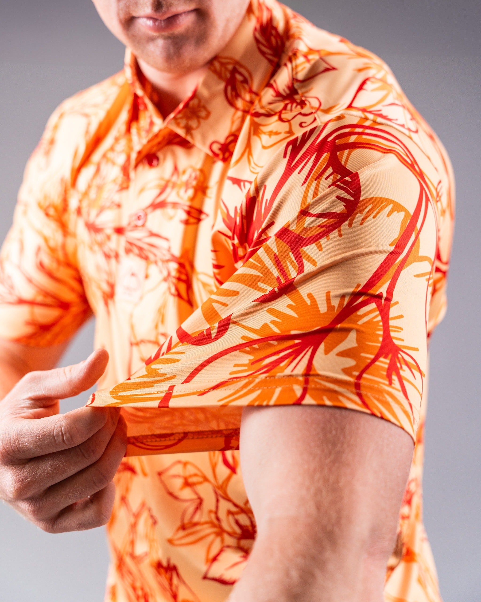 Bold orange and yellow floral golf shirt with short sleeves, showcasing vibrant sunburst design on a model.