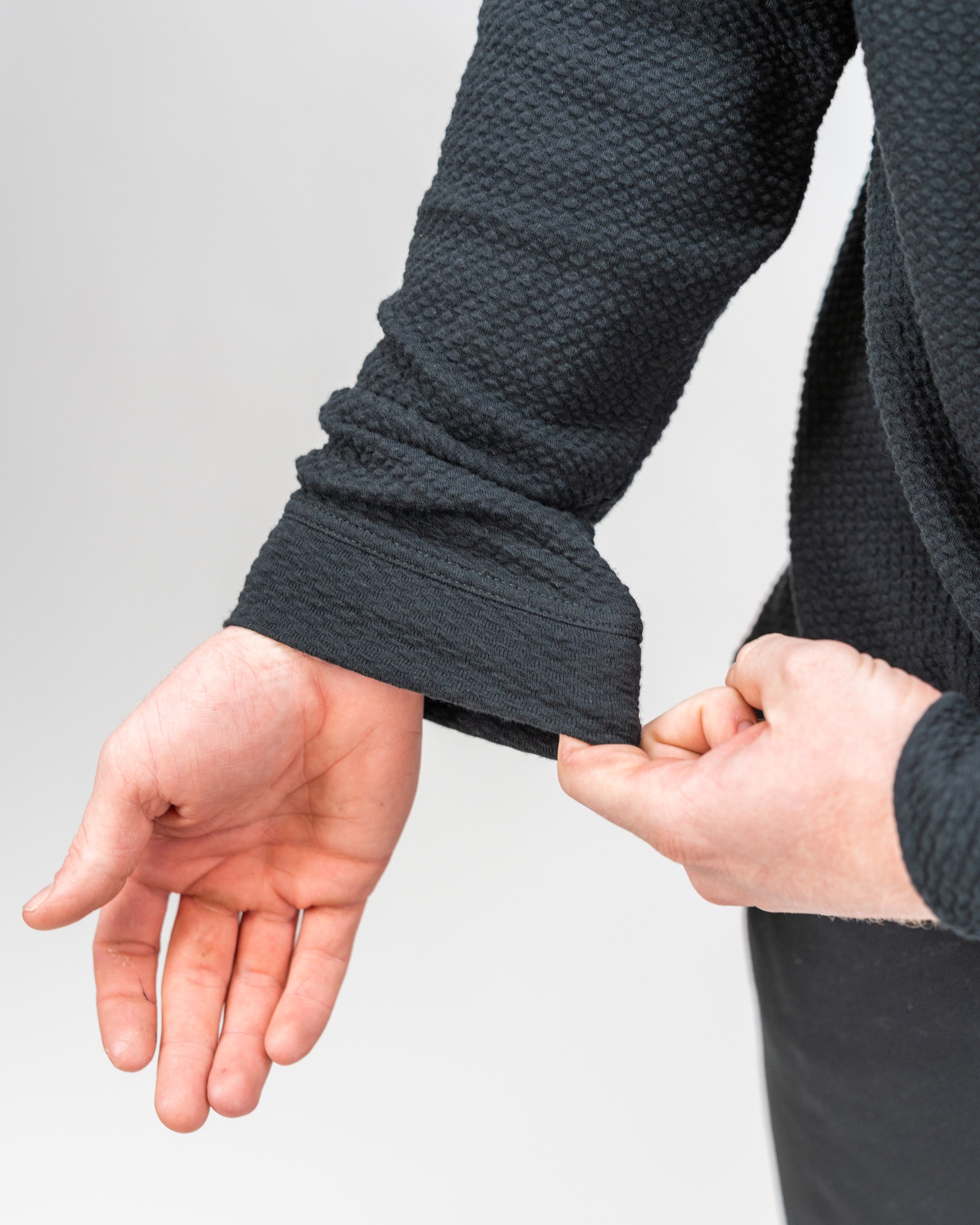 Close-up of a hand adjusting the cuff of a Player Preferred waffle knit hoodie in obsidian, showcasing its textured fabric.