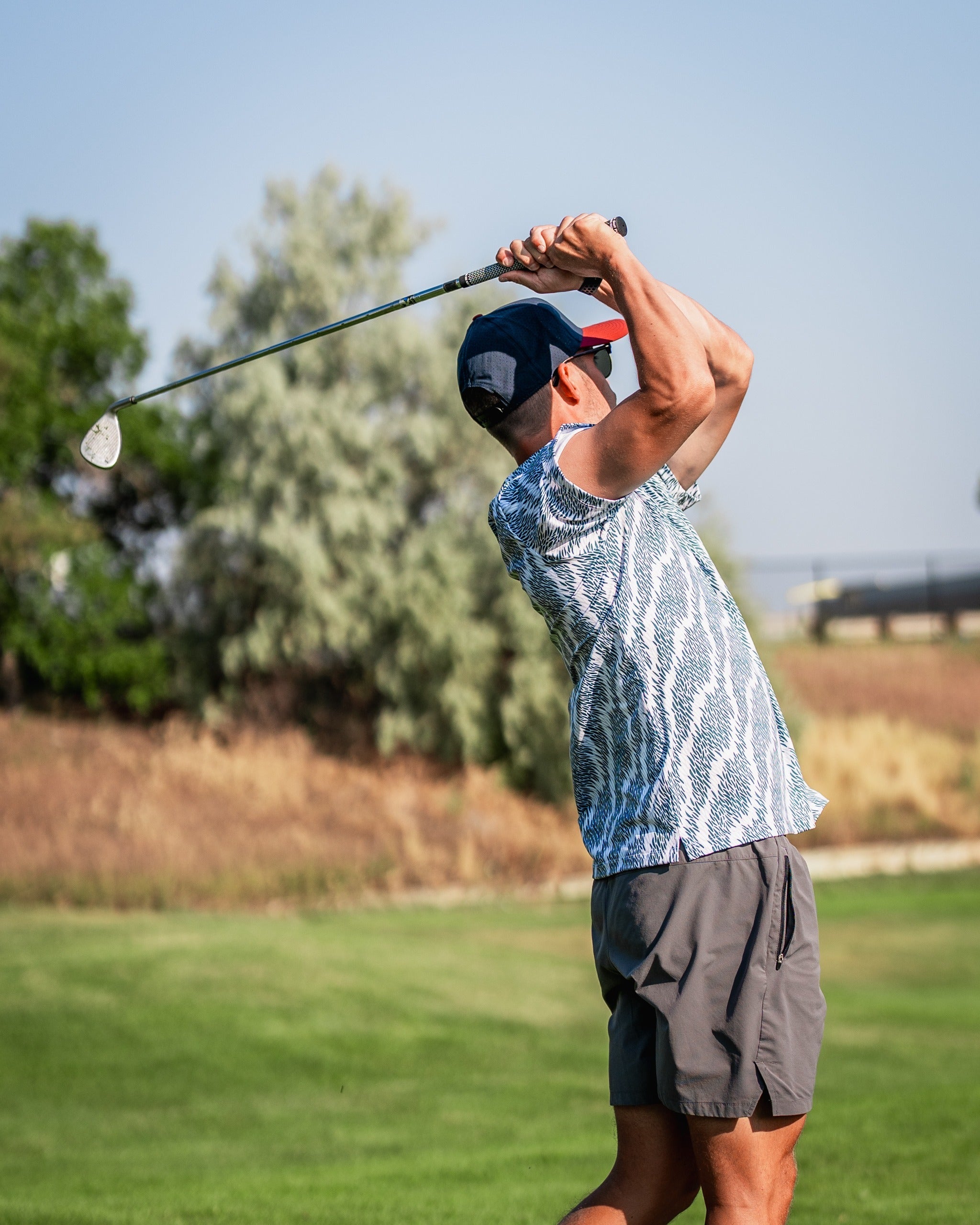 A golfer swings a club on the course, wearing a stylish patterned shirt and shorts, showcasing bold golf apparel.