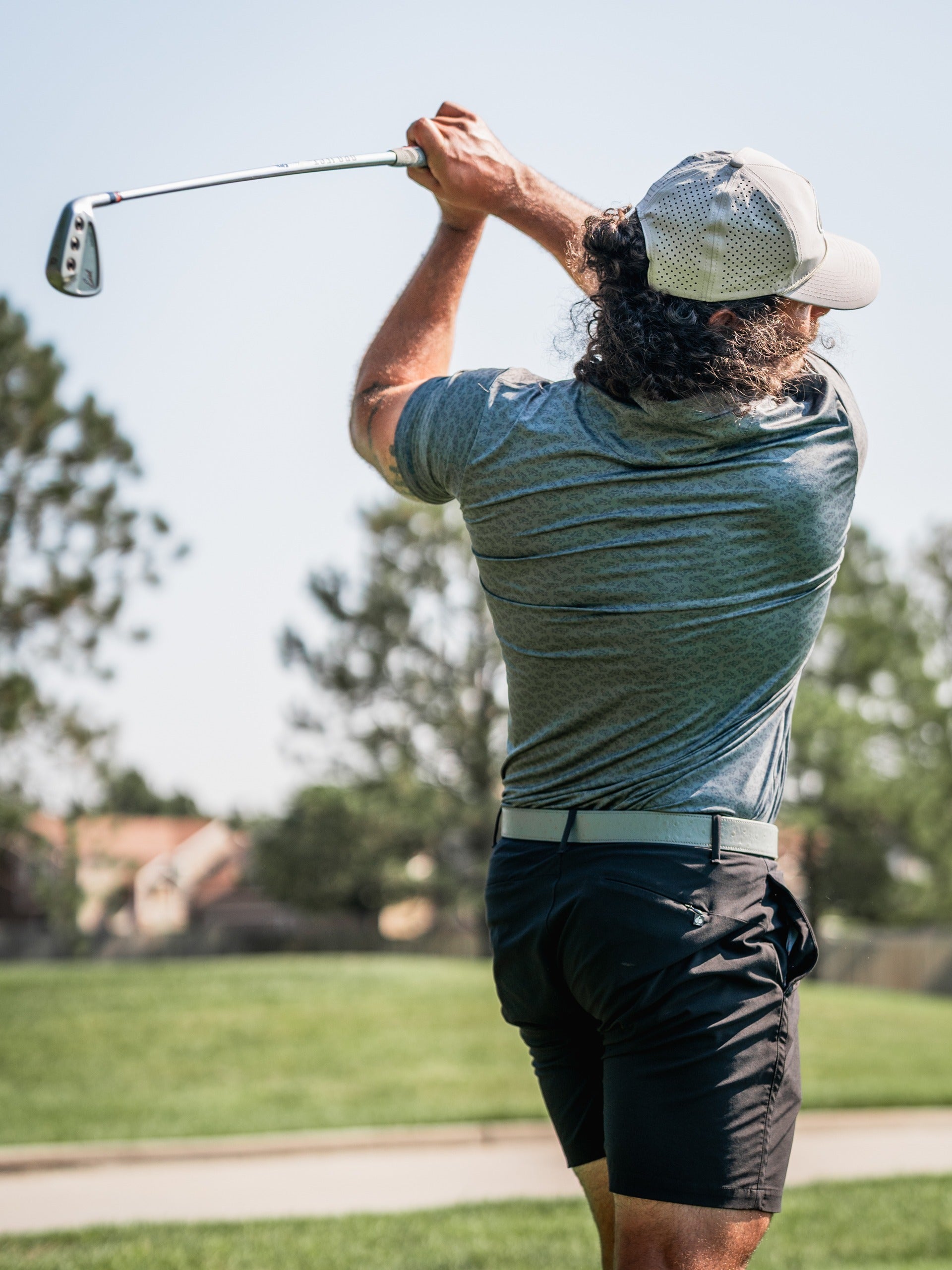 A golfer swings a club on the course, showcasing a stylish gray shirt and black shorts, embodying bold golf fashion.