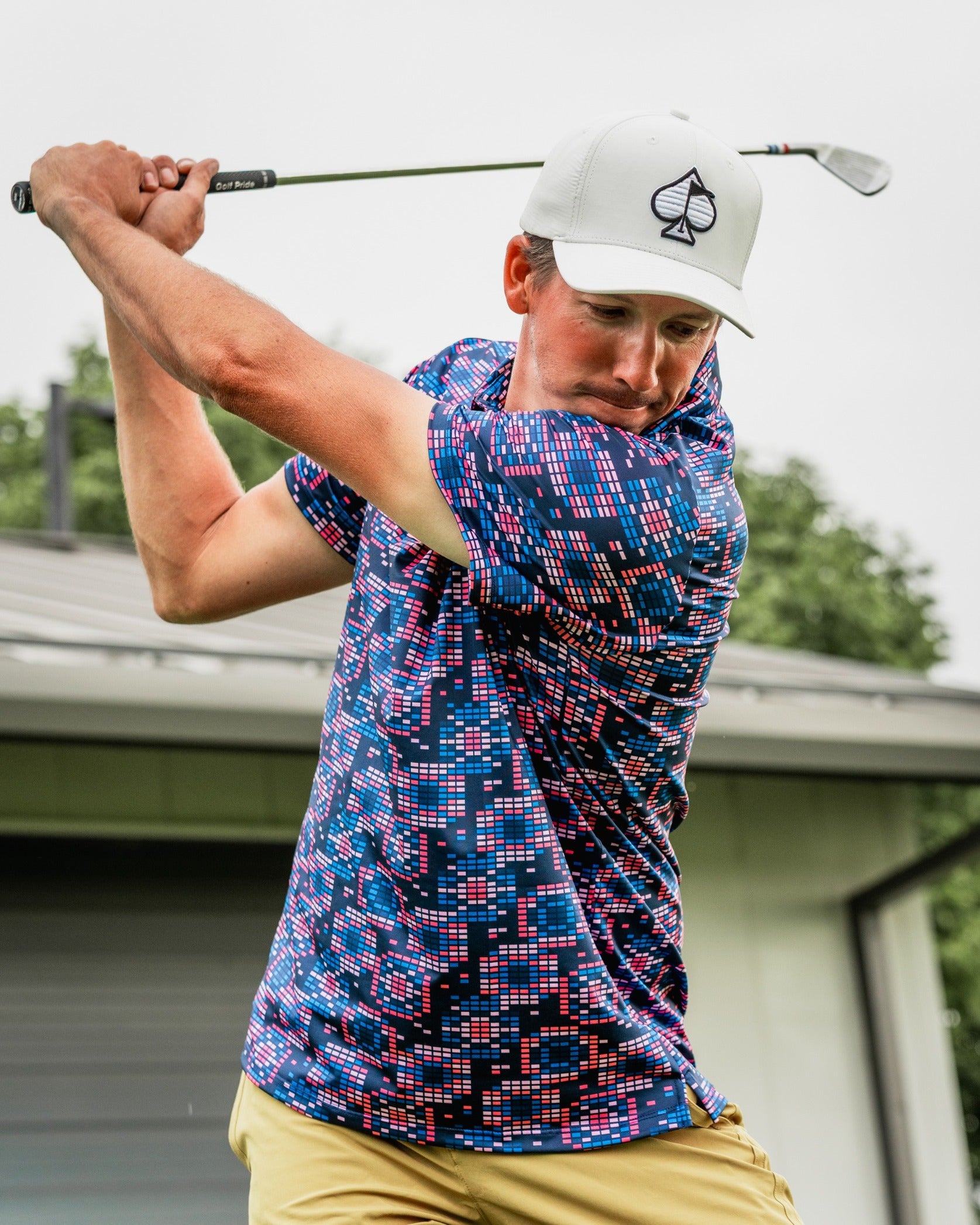 A golfer swings a club while wearing a vibrant Tetrafloral Dark polo shirt featuring a bold geometric pattern.