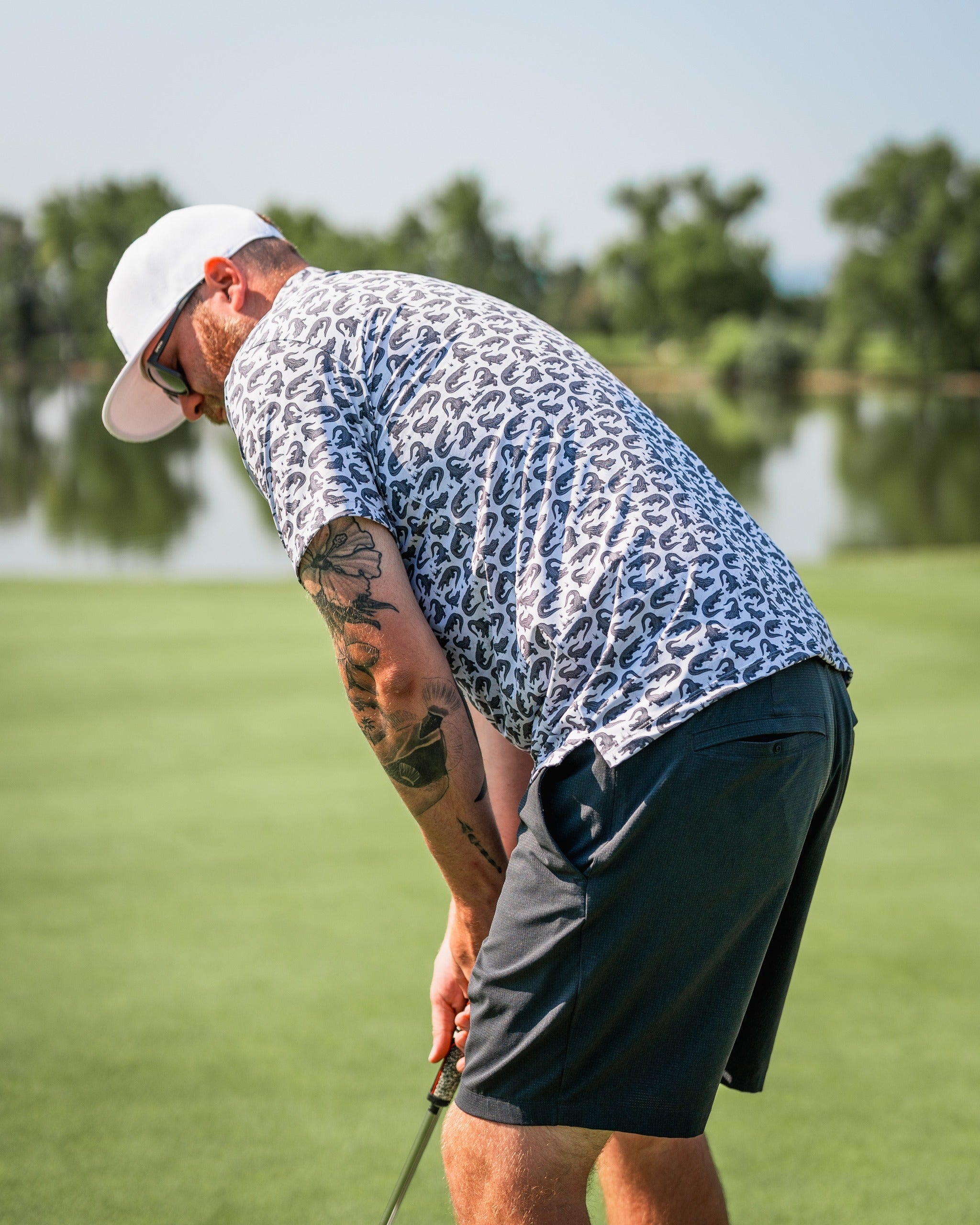 A golfer wearing a bold leopard print polo shirt and shorts, putting on a green course with trees in the background.