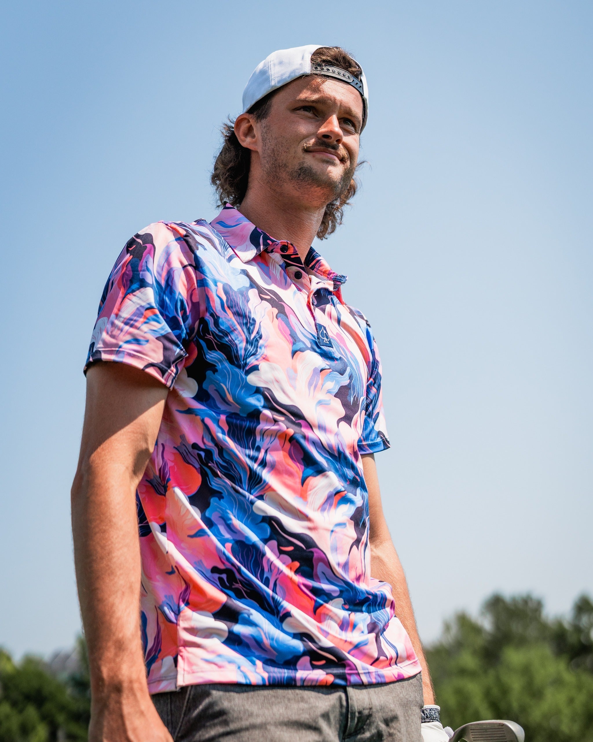 A golfer wearing a vibrant melting floral polo shirt, standing confidently on the course under a clear blue sky.