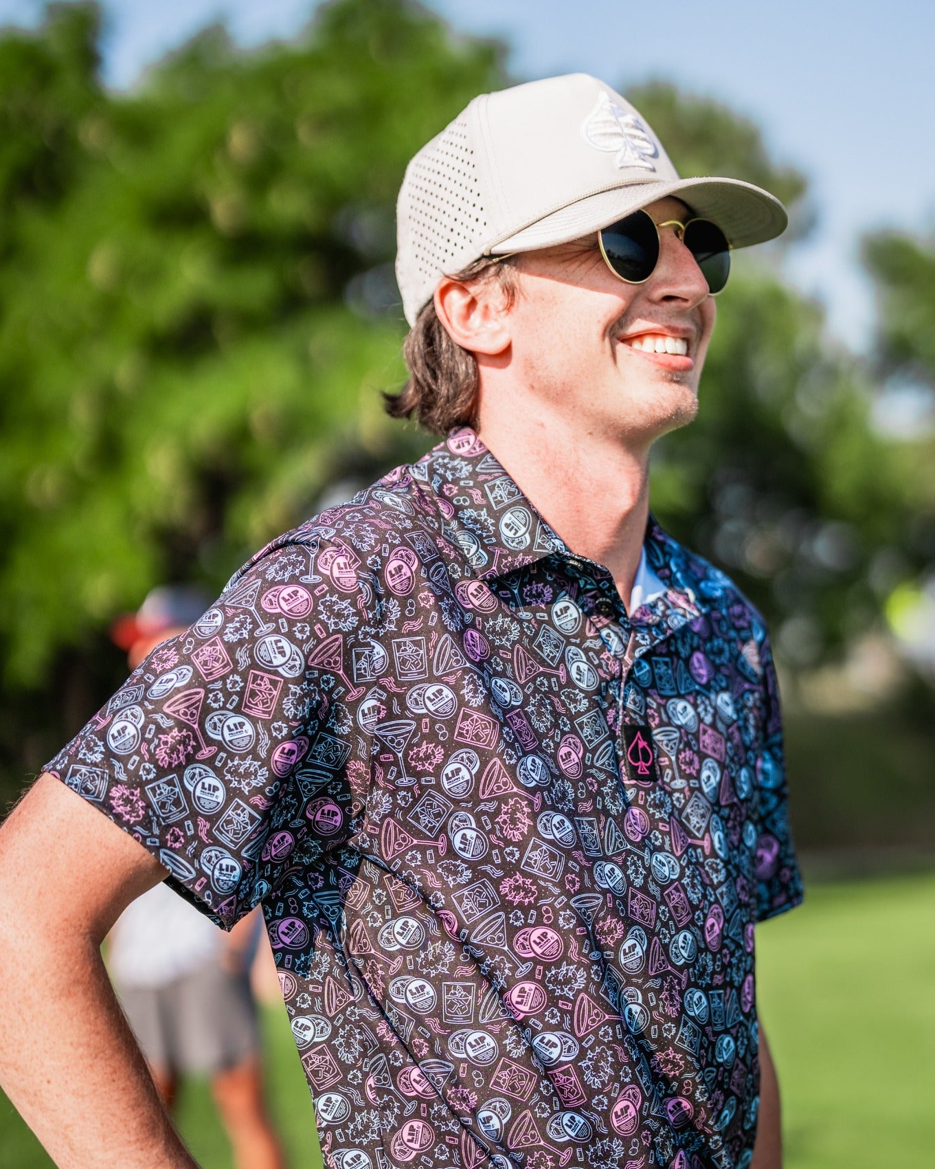 A golfer wearing a colorful Lip Pillows shirt, smiling on the course with sunglasses and a cap.