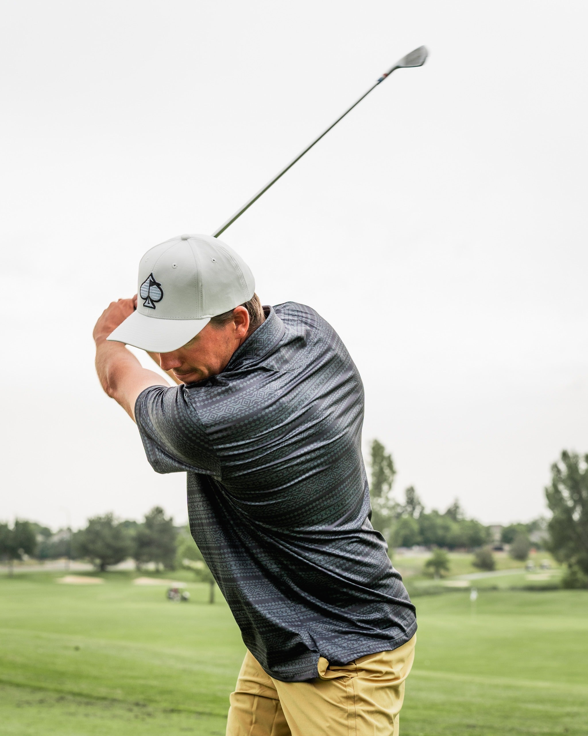 A golfer swings a club on the course, wearing the Desert Geo polo shirt and a matching cap, showcasing bold golf style.