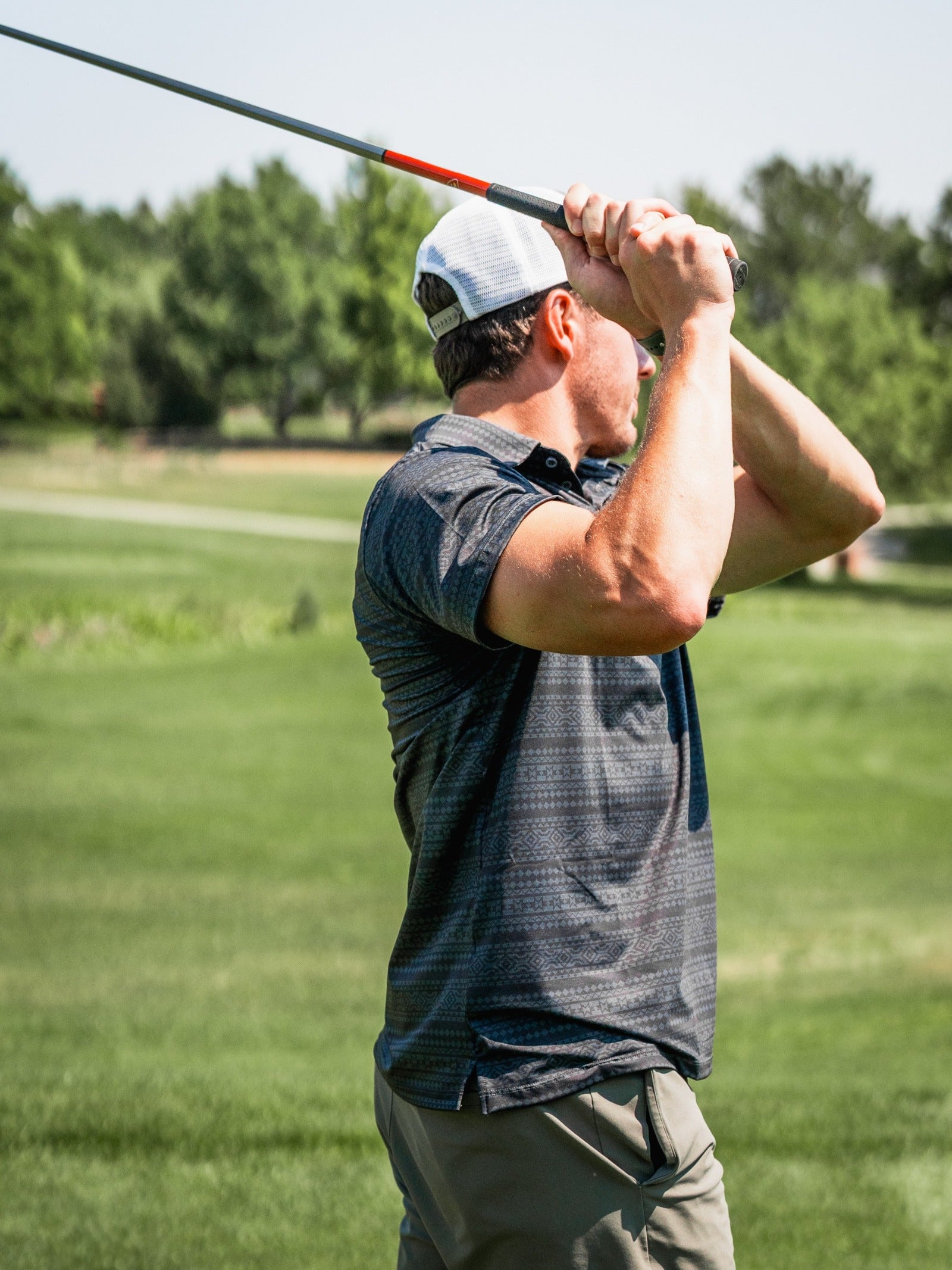 A golfer in a stylish Desert Geo polo shirt prepares to swing on a sunny course, showcasing bold patterns and a modern fit.