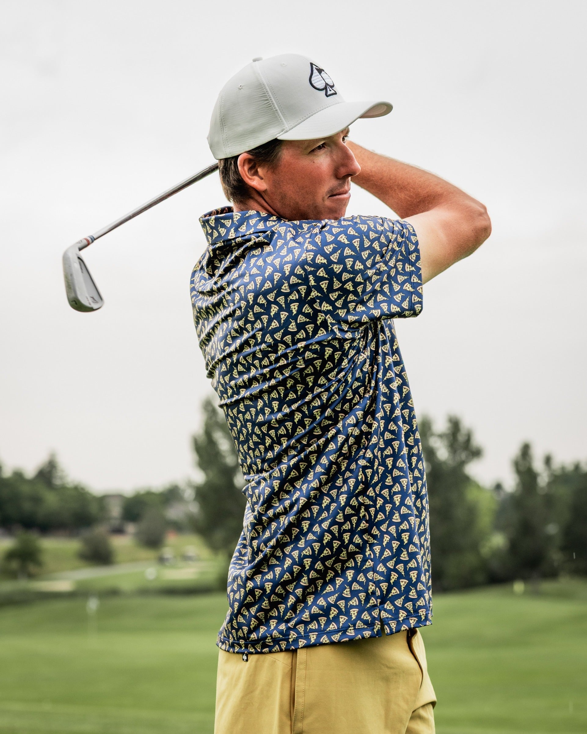 Golfer in a patterned shirt swings a club on the course, showcasing bold golf apparel and a stylish cap.