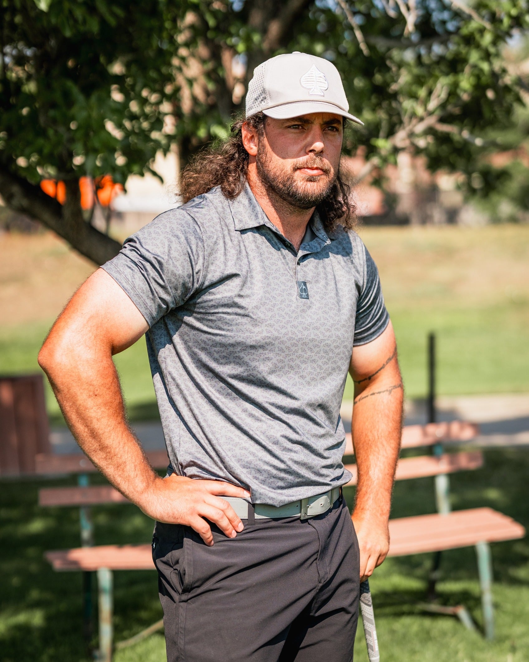 A golfer wearing a gray patterned polo and a cap stands confidently on the course, showcasing bold golf apparel.