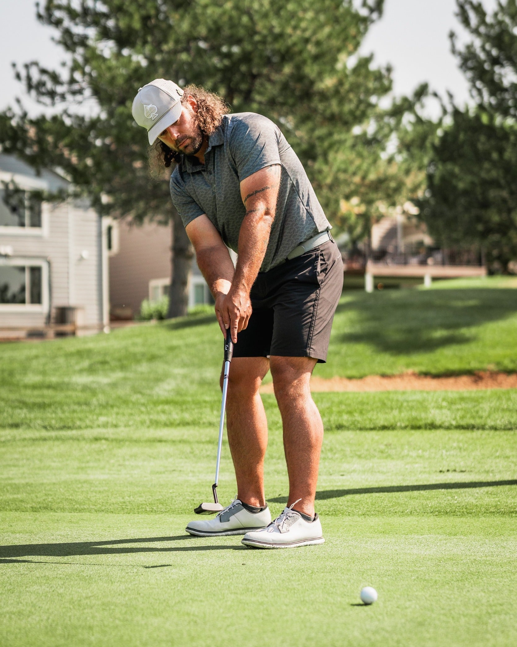 Golfer in a gray polo and black shorts putts on a lush green course, showcasing the Large Mouth golf accessory.
