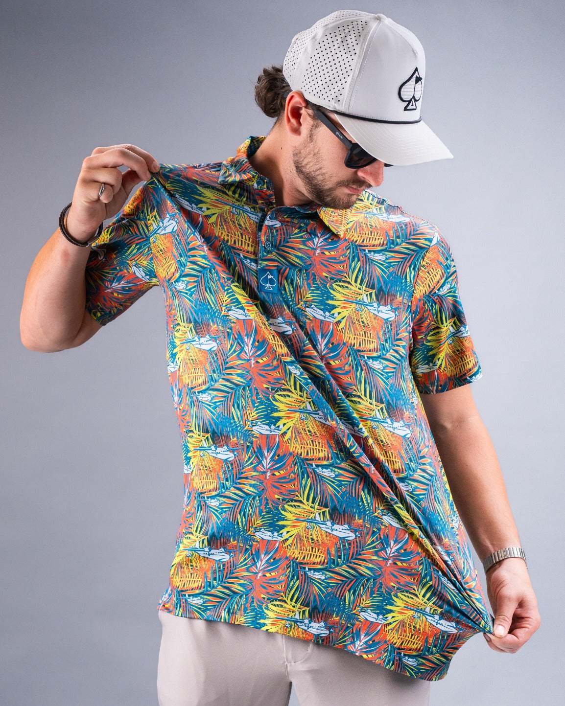 A man showcases a colorful Margaritaville Bama Breeze polo shirt featuring vibrant tropical patterns against a gray background.