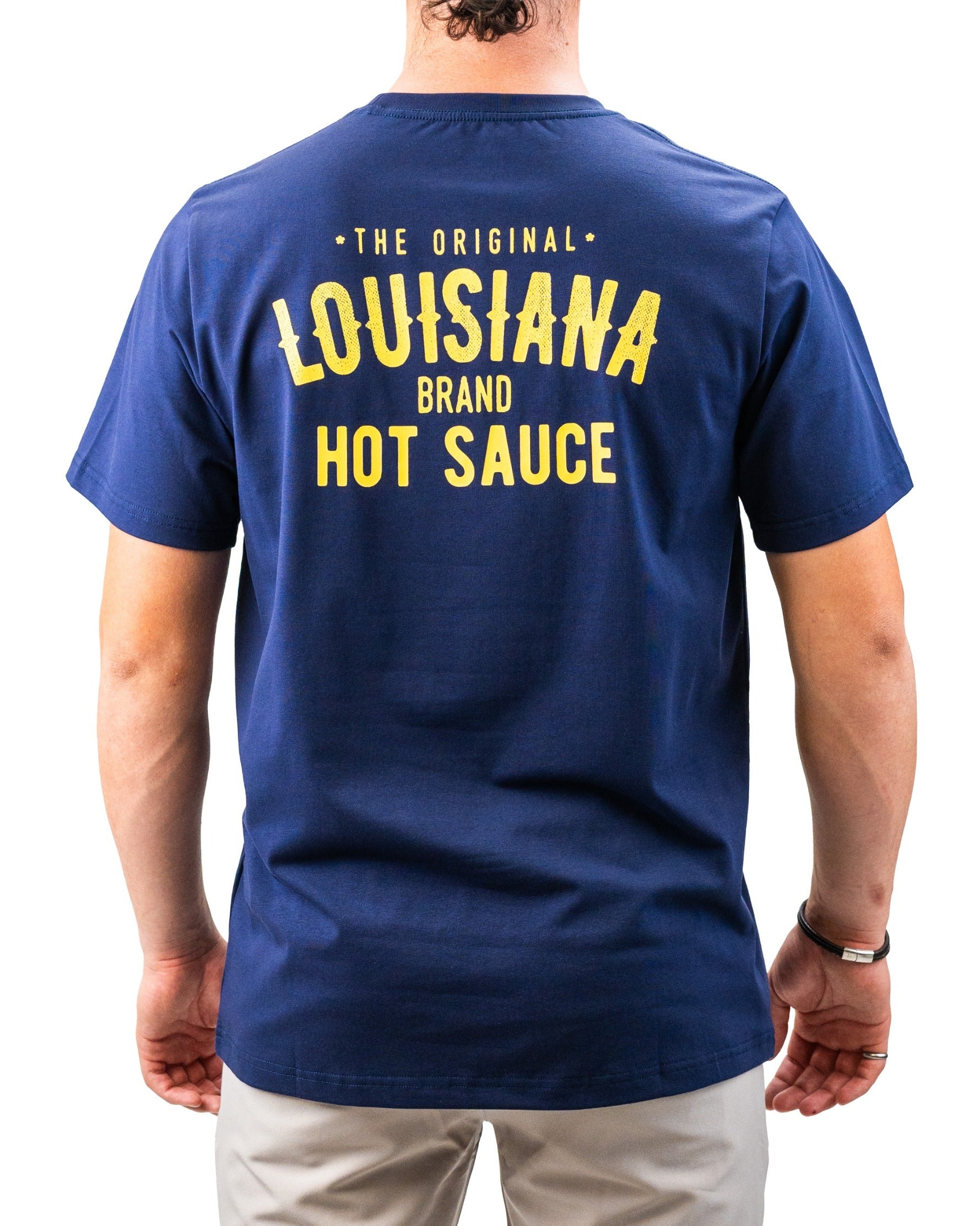 Back view of a navy blue golf t-shirt with bold yellow text reading "Louisiana Brand Hot Sauce" and "The Original" at the ...