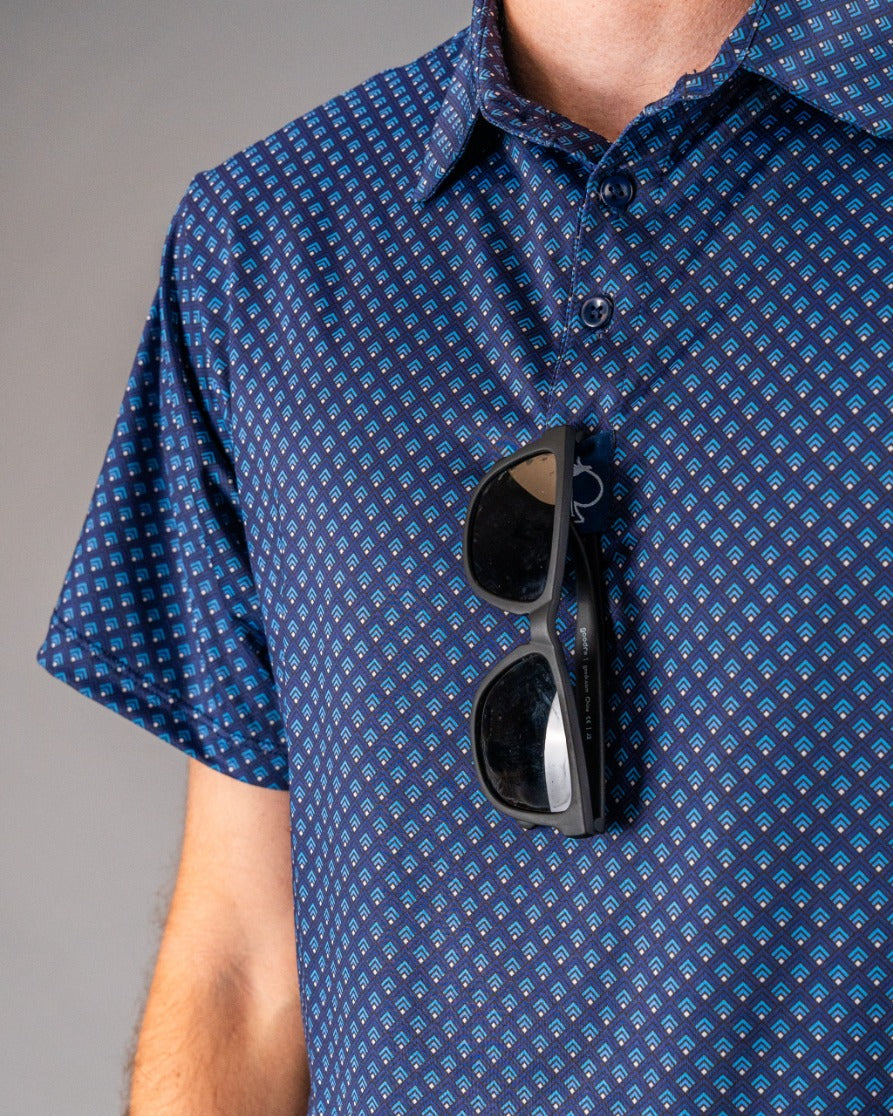 Black sunglasses clipped to a blue patterned golf shirt with small geometric designs, perfect for bold golf style.